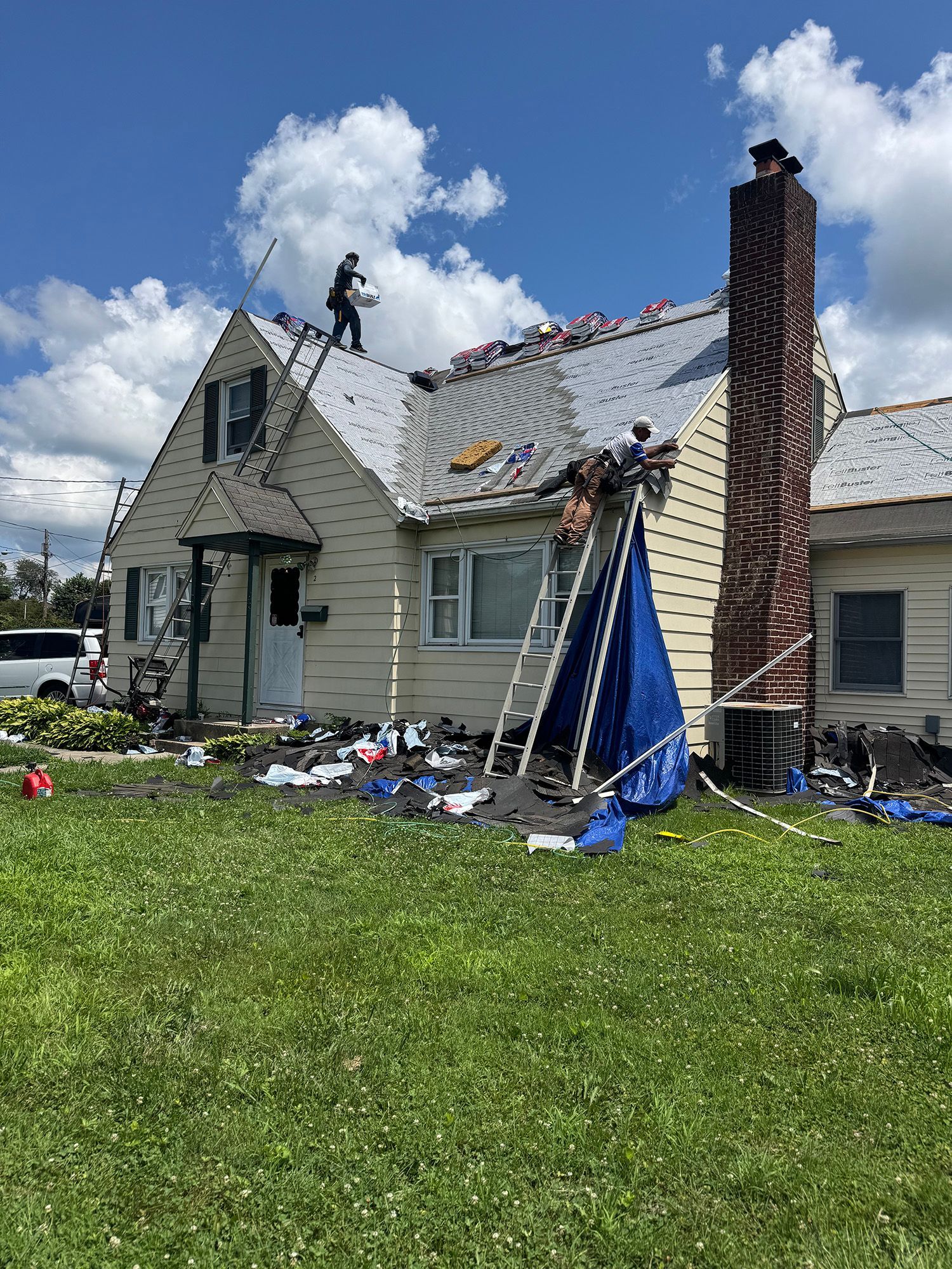 Roofers working on a residential house, debris on the ground, sunny day.