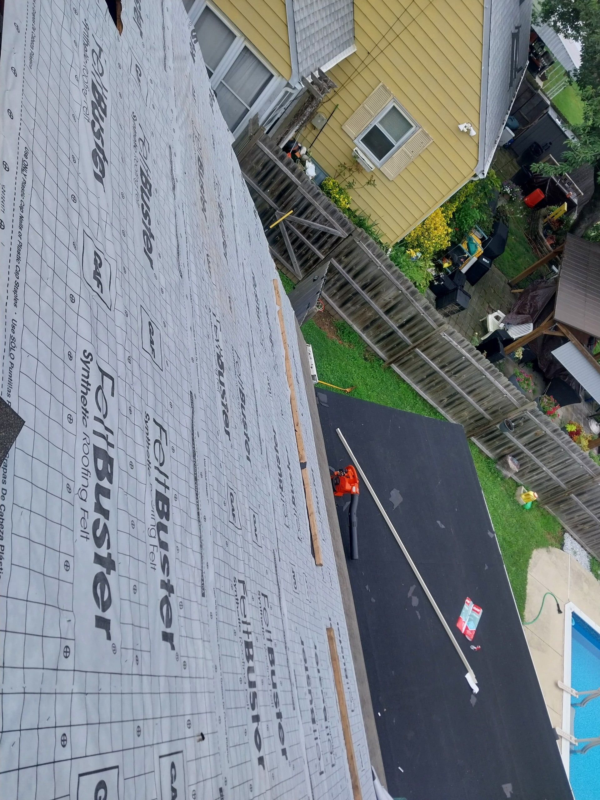 Rooftop with new underlayment, view of a yard with a pool and neighboring house.
