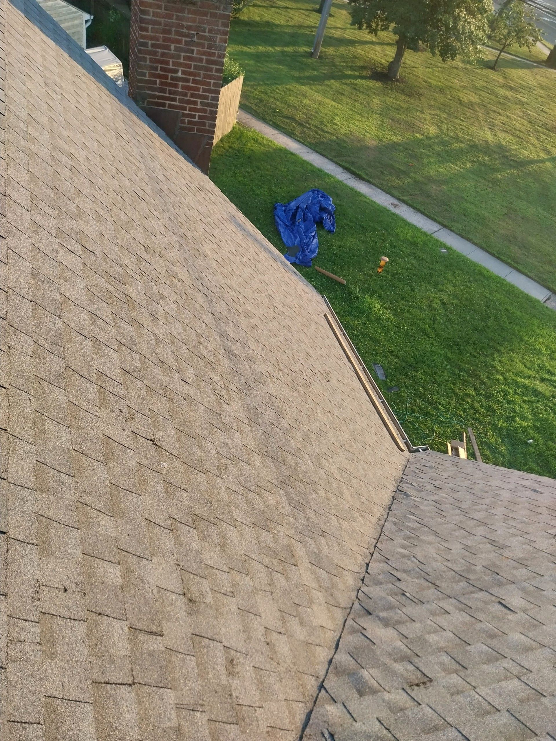 A roof with shingles, a brick chimney, and a lawn with a blue tarp in view.