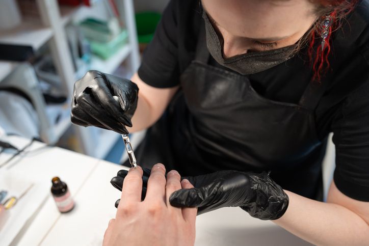 Manicurist in black gloves applying cuticle oil