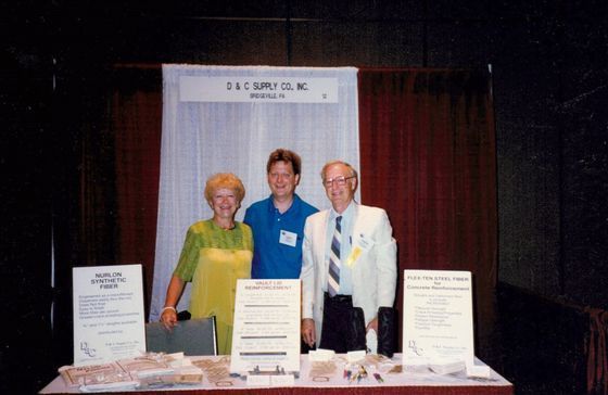 Three people standing behind a display table at a booth, with informational posters and brochures.