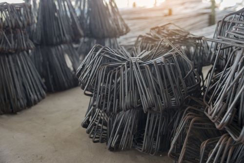 Stacks of bent metal rebar frames piled outdoors on a concrete surface.