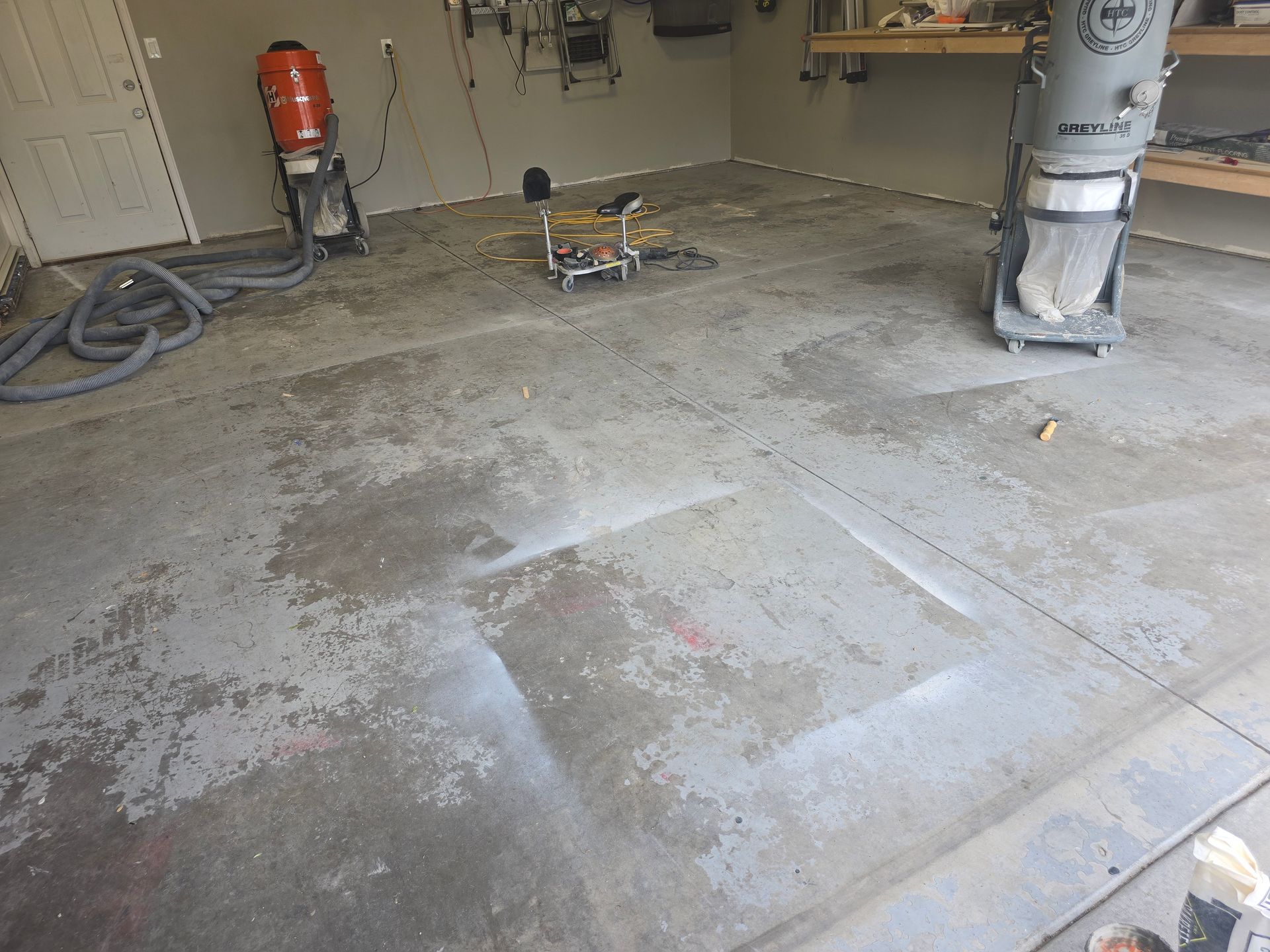 Garage floor being prepped for refinishing, with grinding equipment and concrete dust.
