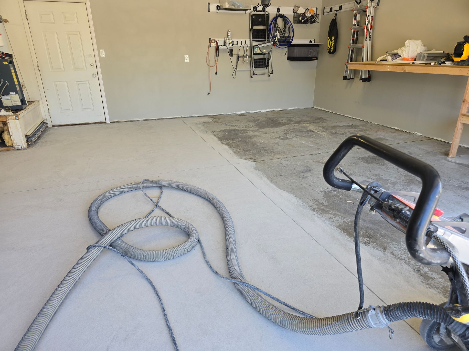 A garage with a floor being resurfaced. A machine is laying down a gray coating on the concrete floor.