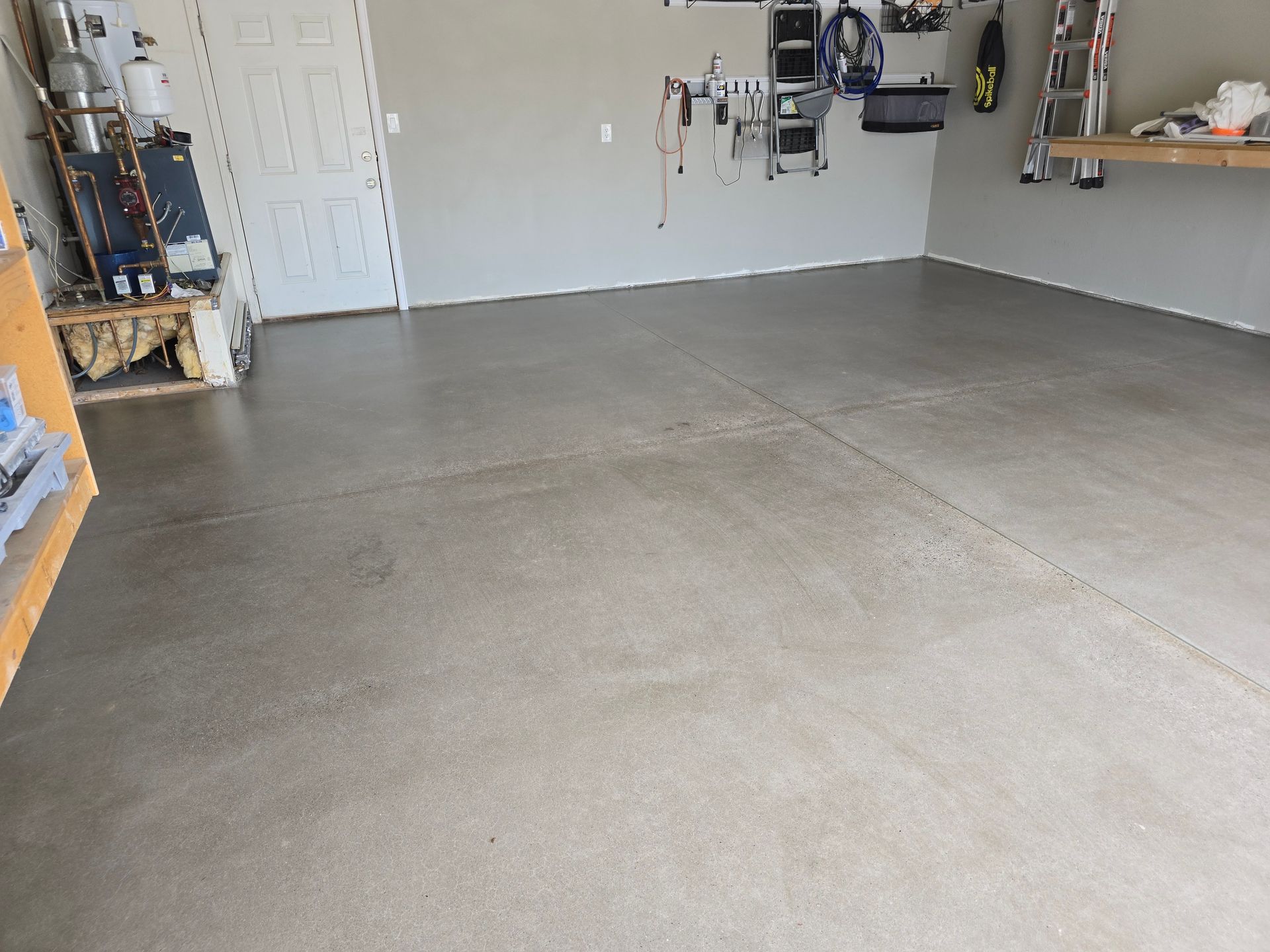 Empty garage with gray concrete floor and walls, white door, and tools.