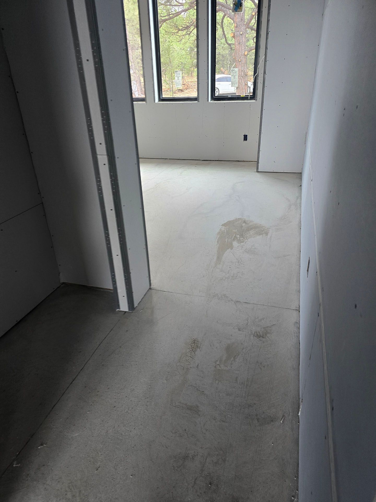 Hallway with concrete floor, leading to a room with windows. Walls are unfinished drywall.