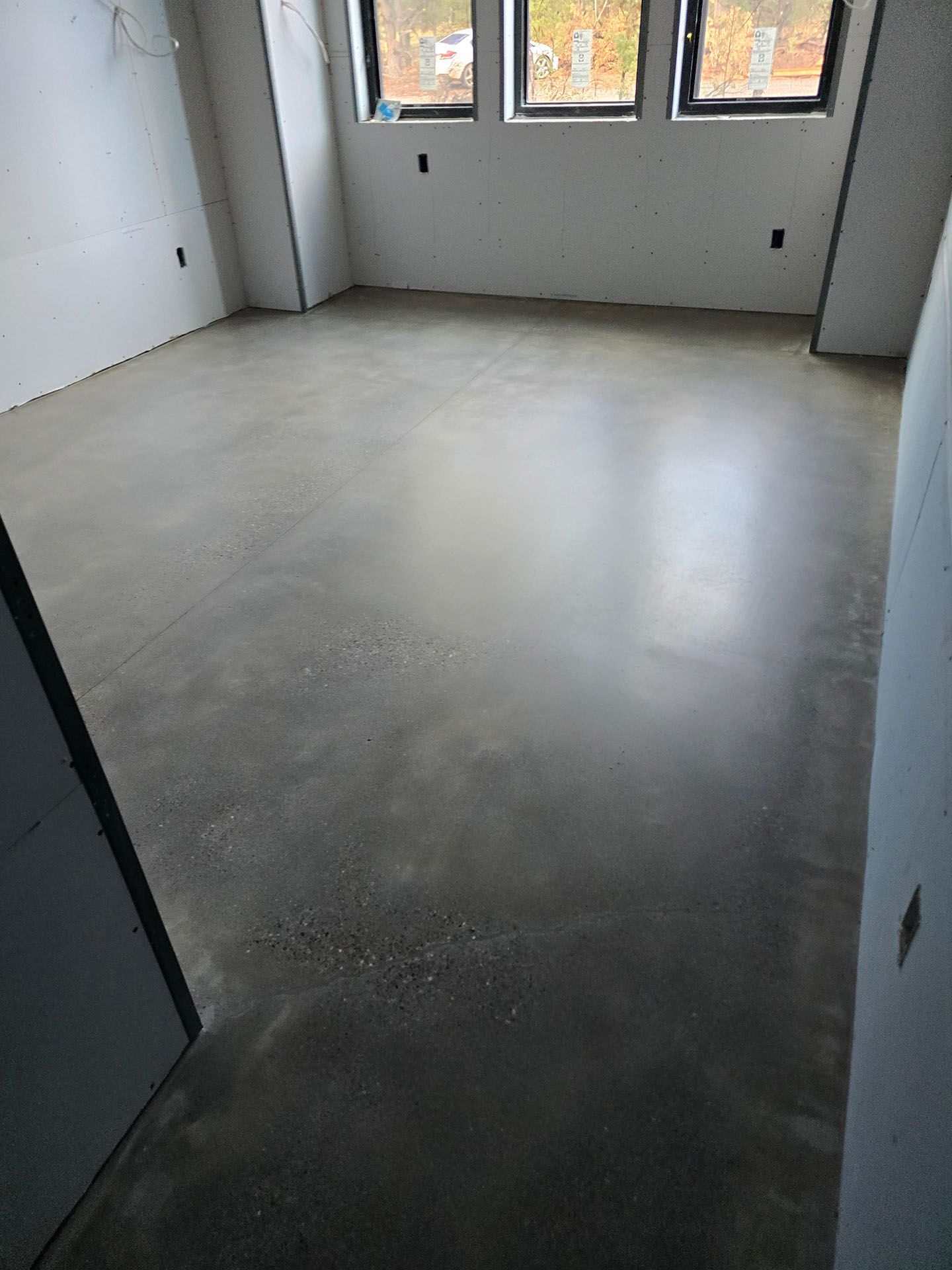 Empty room with polished concrete floor. Three windows provide natural light.