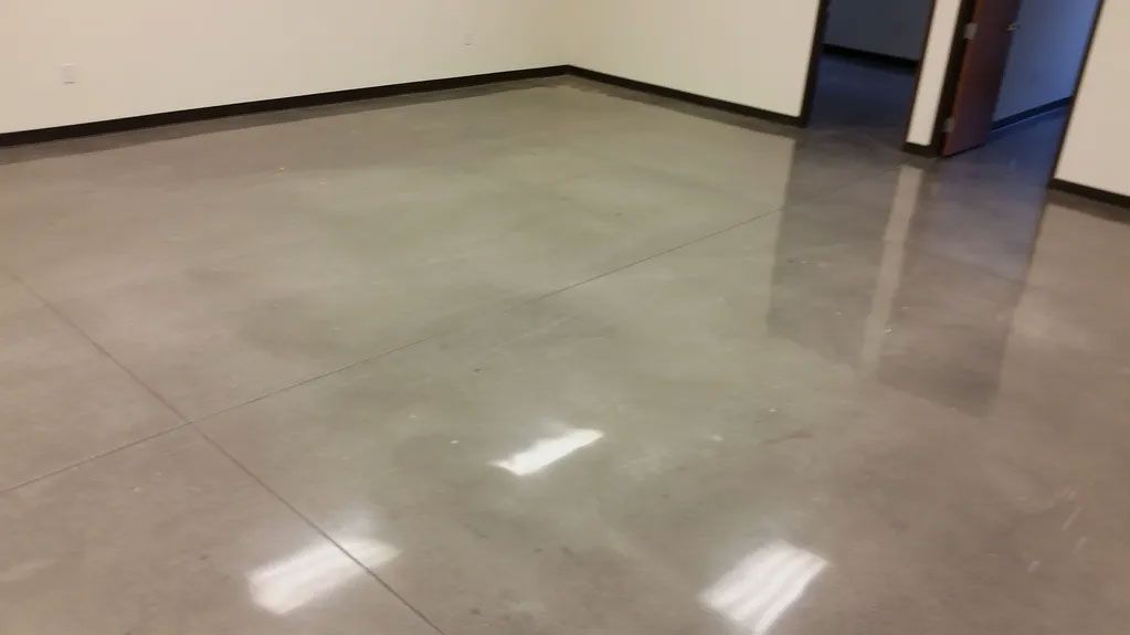 Polished concrete floor in a room, reflecting overhead lights, near a doorway.
