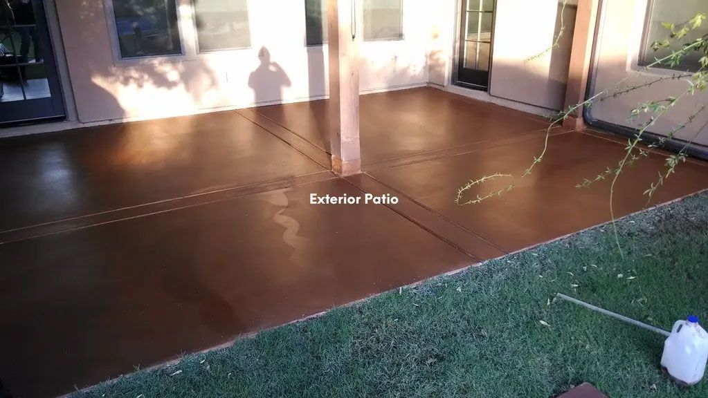 Brown stained concrete patio with a support beam, grass, and a building in the background.