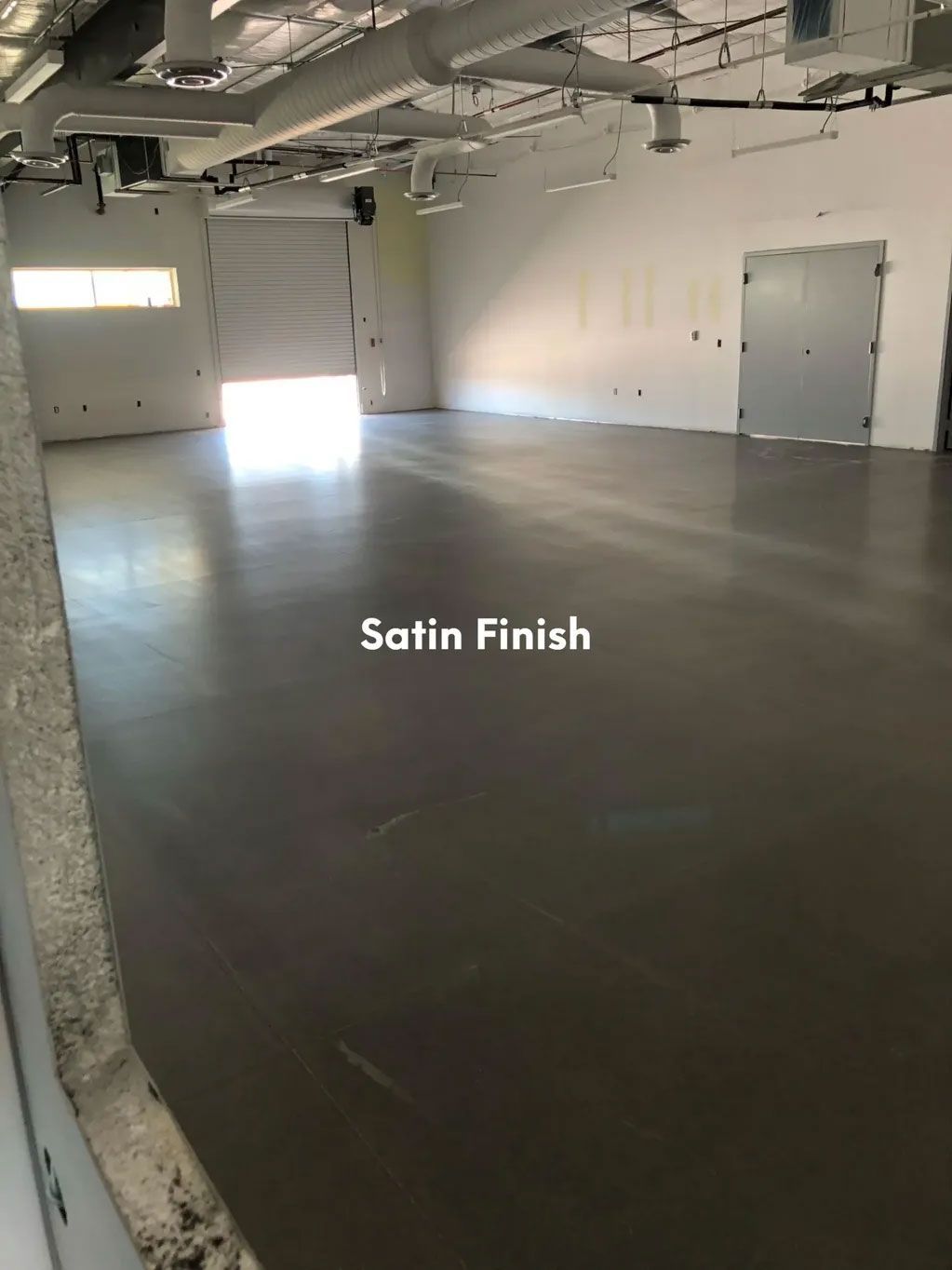 Empty room with a satin-finished gray floor, overhead lighting, and closed garage door.