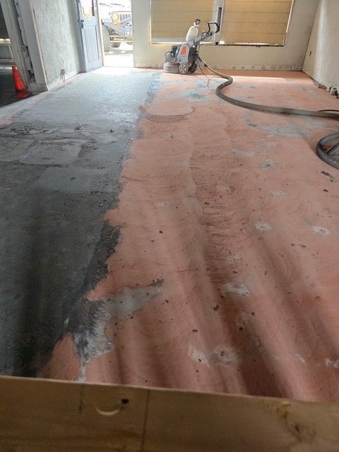 Floor being ground, with a person operating a machine. Sections are raw concrete and coated with orange material.