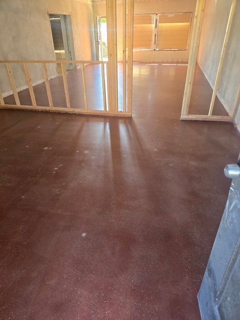 Brown stained concrete floor in a room under construction, with wooden framing and partial railing.