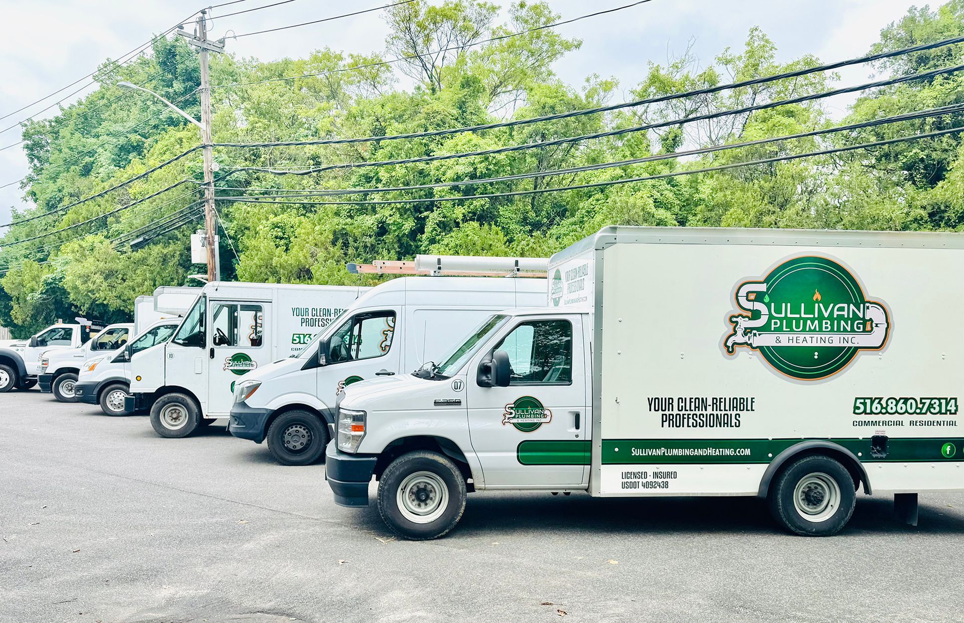 A row of plumbing trucks are parked in a parking lot.