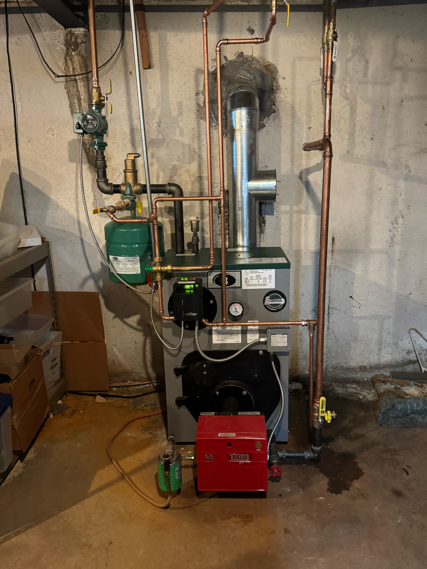A boiler is sitting in a basement surrounded by pipes.