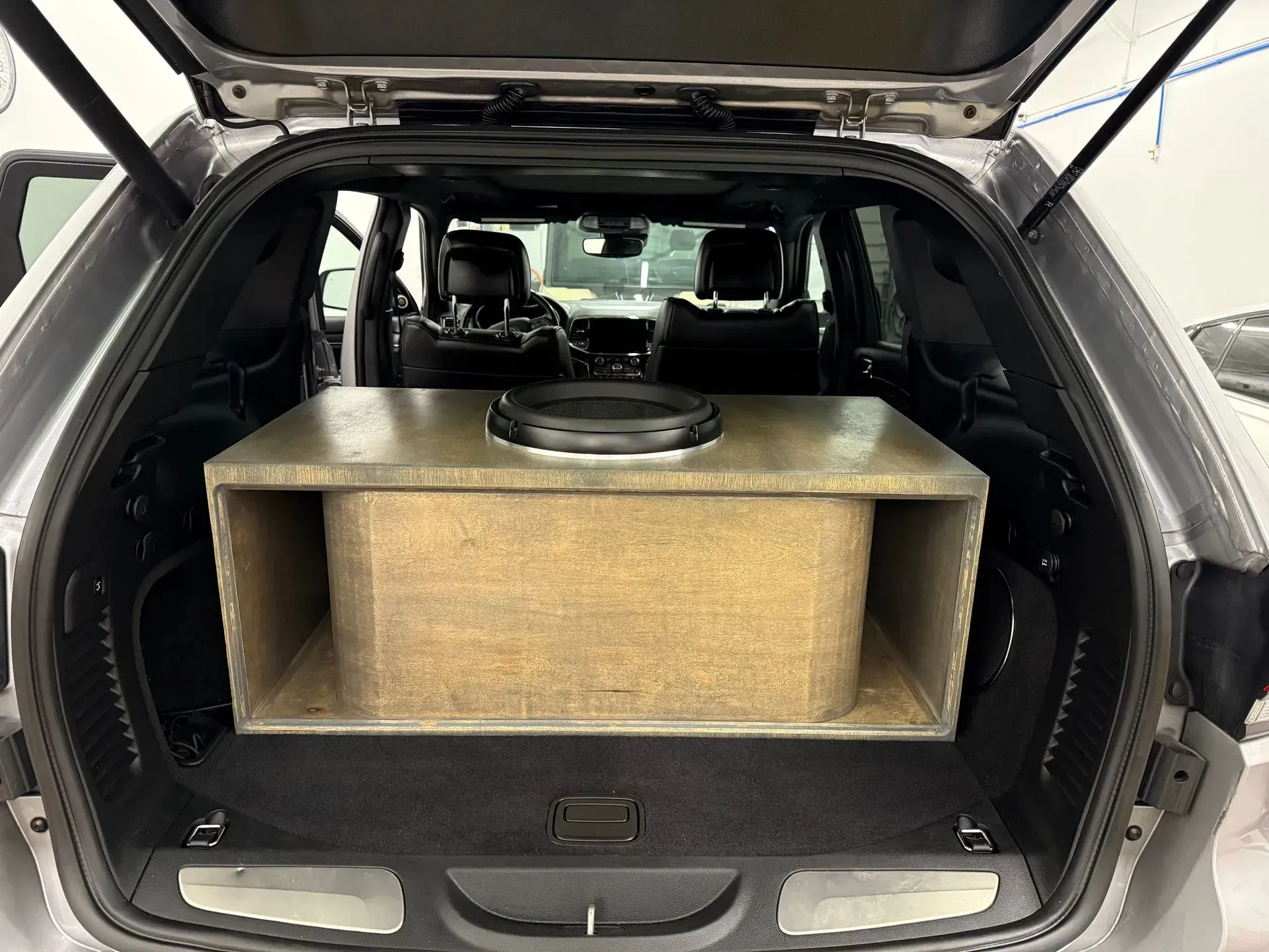 A vehicle's trunk with a large speaker box containing a subwoofer installed.