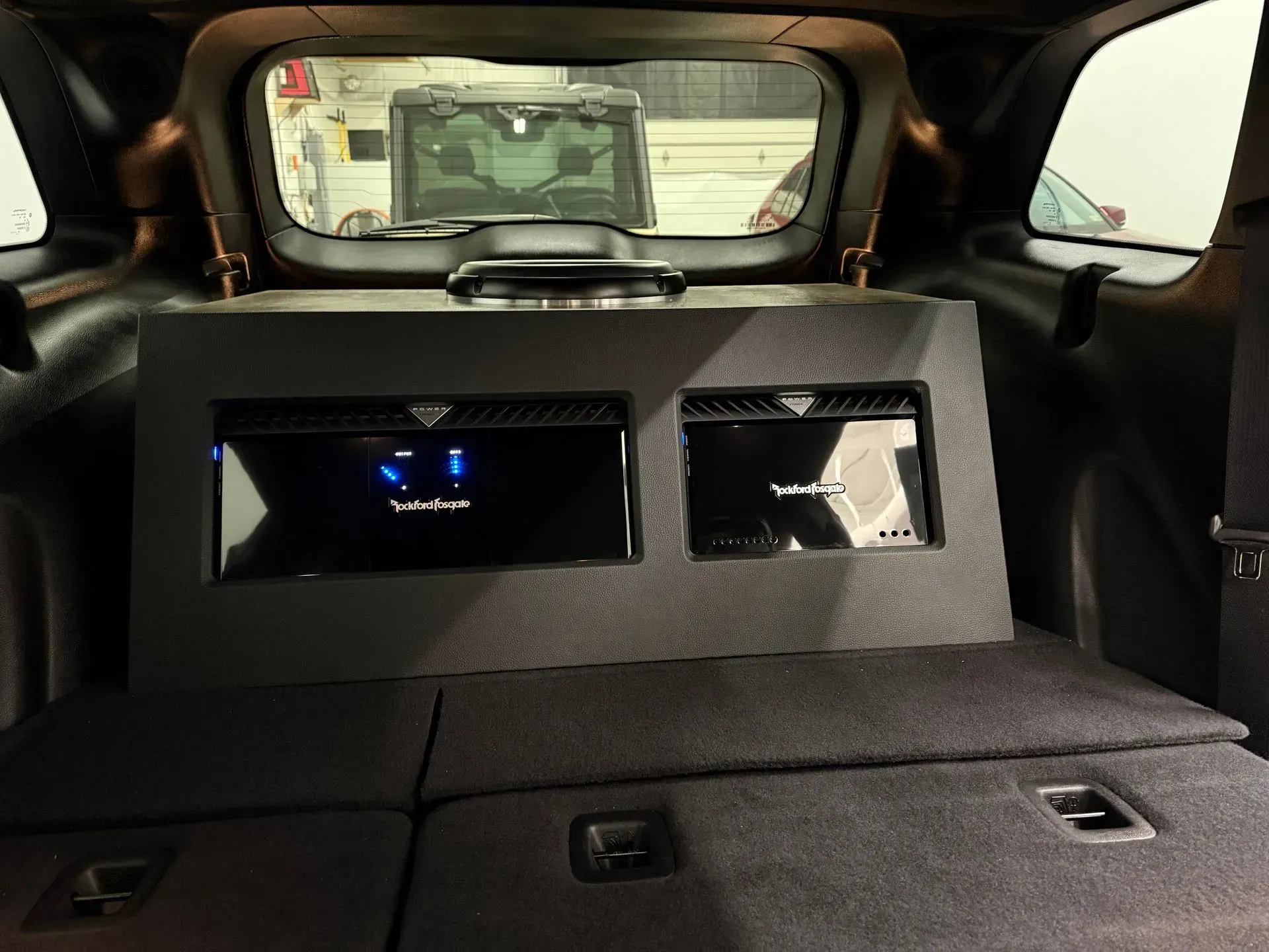 Car trunk interior with two black audio amplifiers mounted on a black panel.