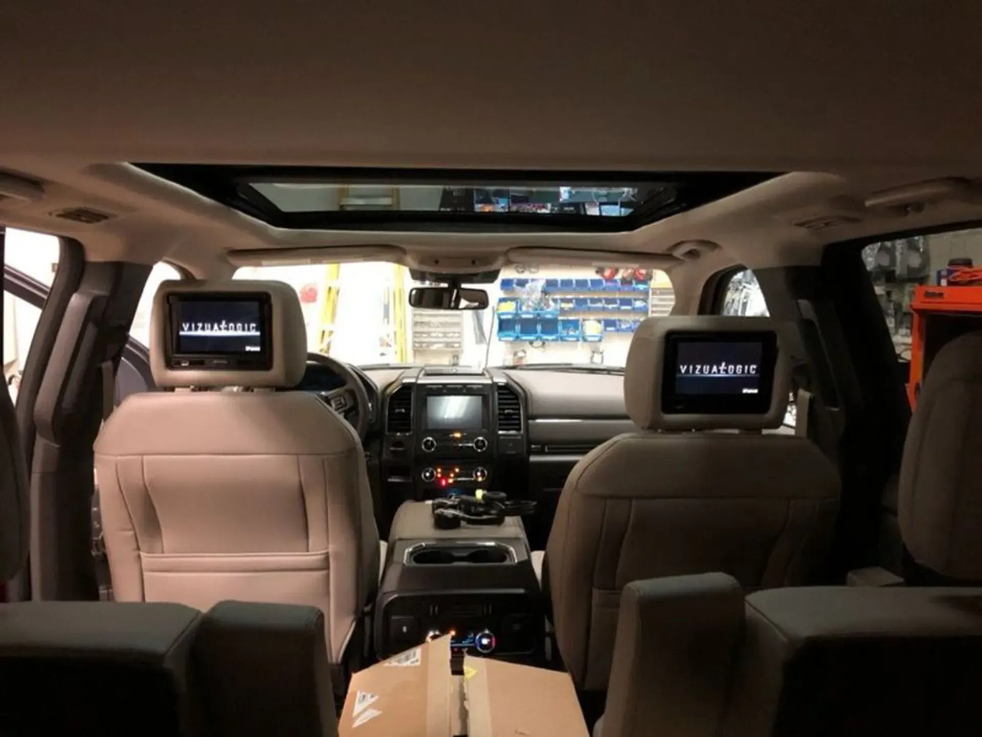 Interior view of a beige SUV with two headrest screens installed; sunroof open.