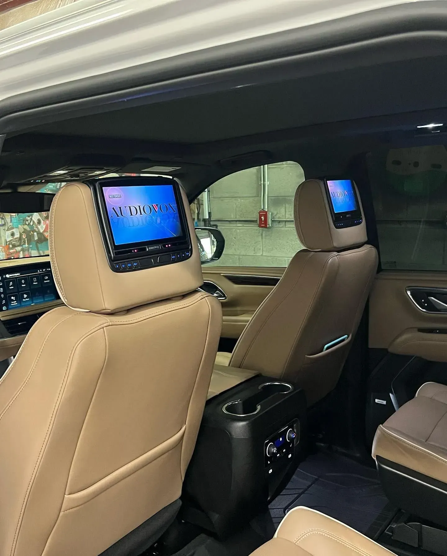 Rear interior of a vehicle with tan seats and two headrest-mounted screens displaying a blue graphic.