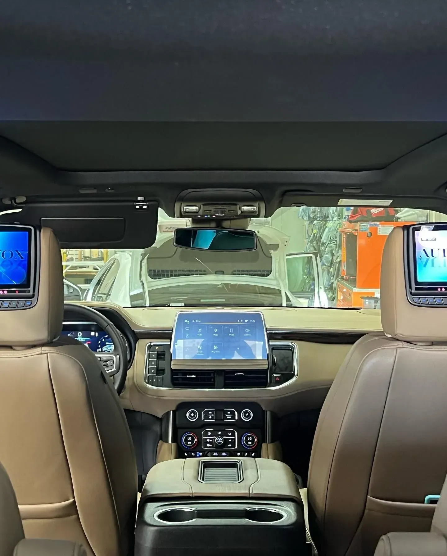 Interior view of a vehicle showing front seats, a touchscreen, headrest screens, and a center console.