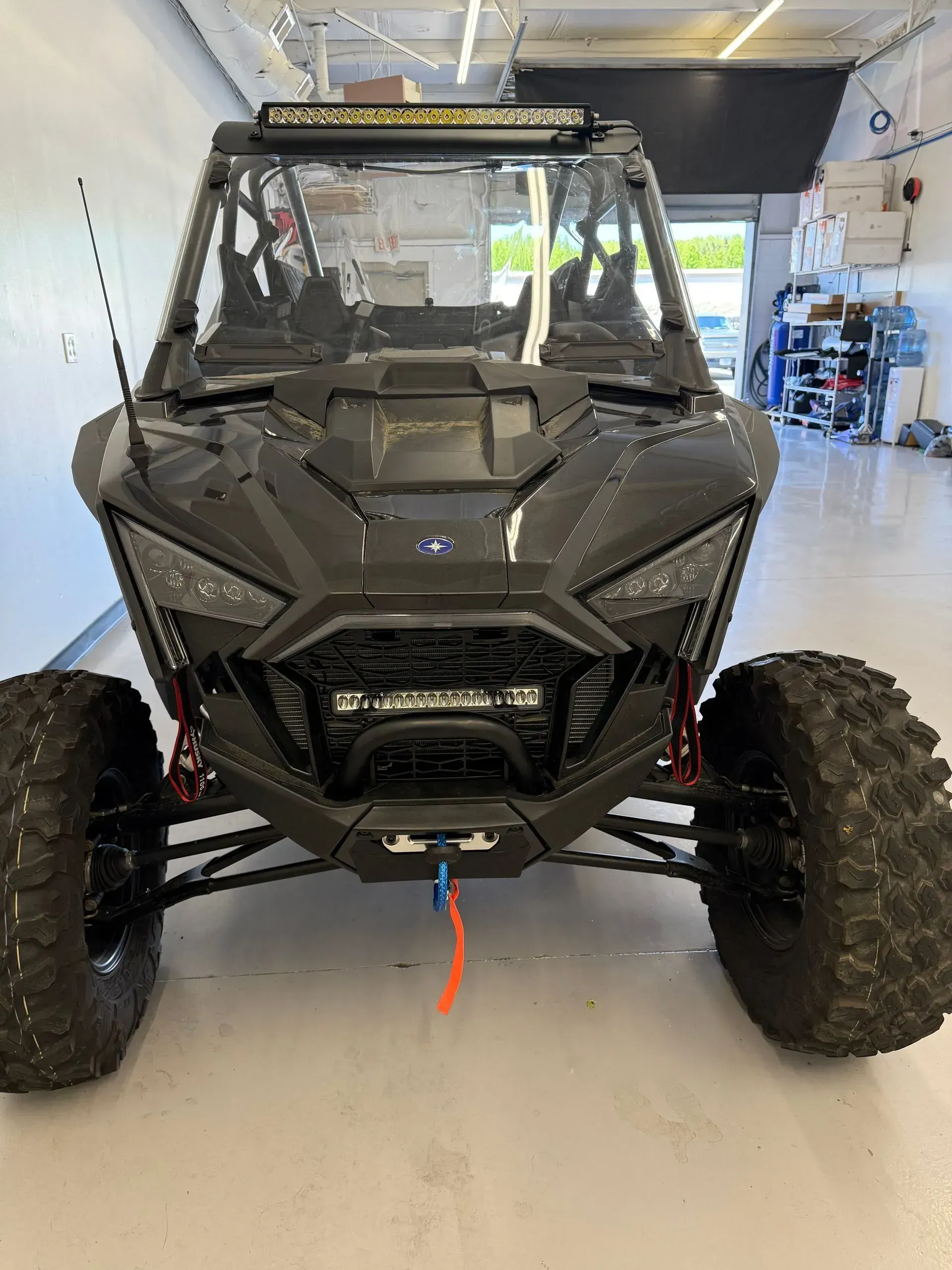 Black Polaris RZR side-by-side UTV with light bar and large tires, parked in a garage.