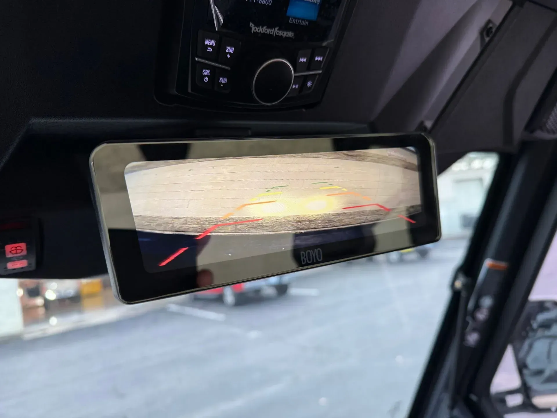 Rearview mirror in vehicle displays a view, red lines, and audio system controls.