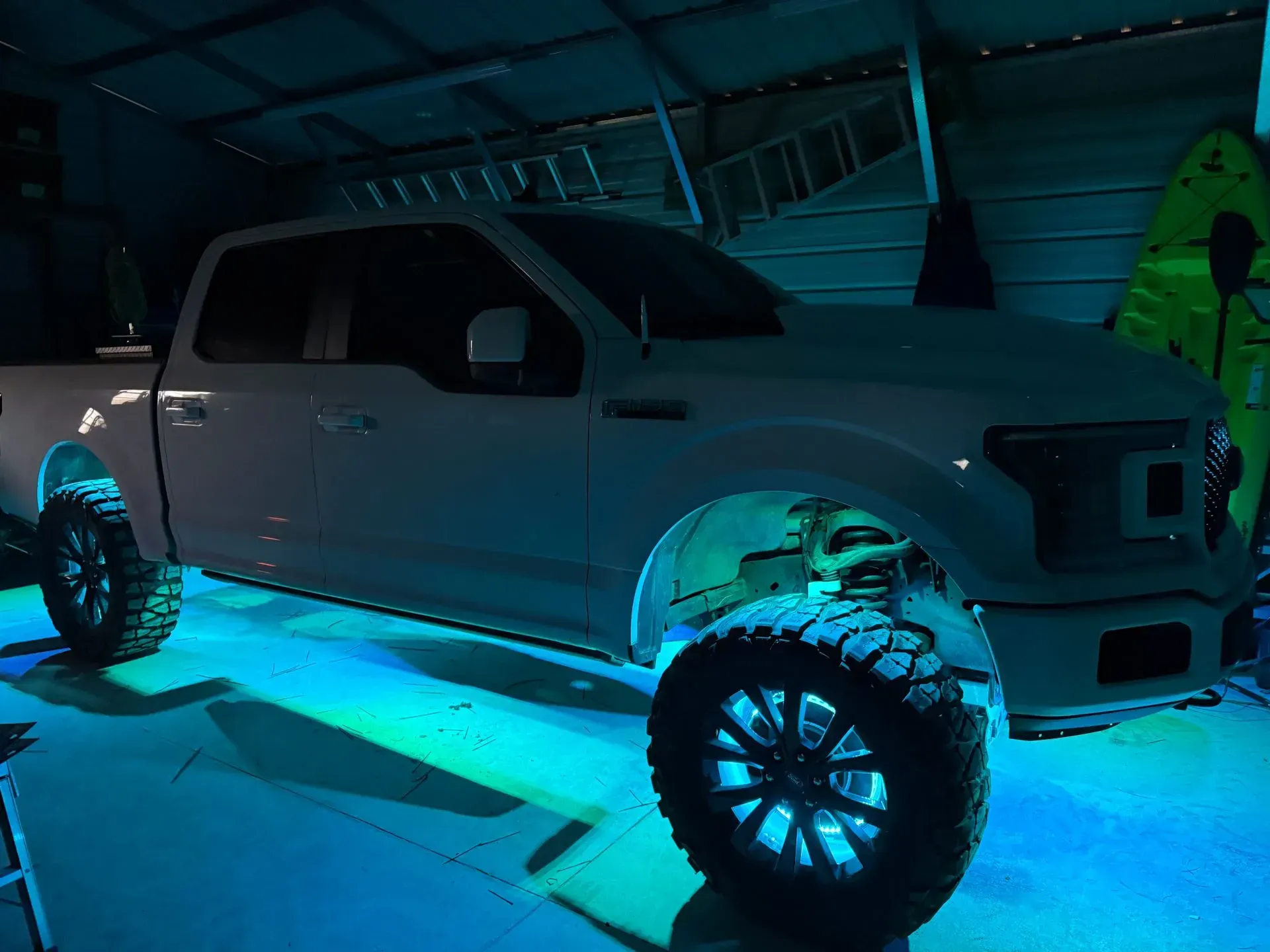 White pickup truck with blue underglow in a garage, showcasing large tires.