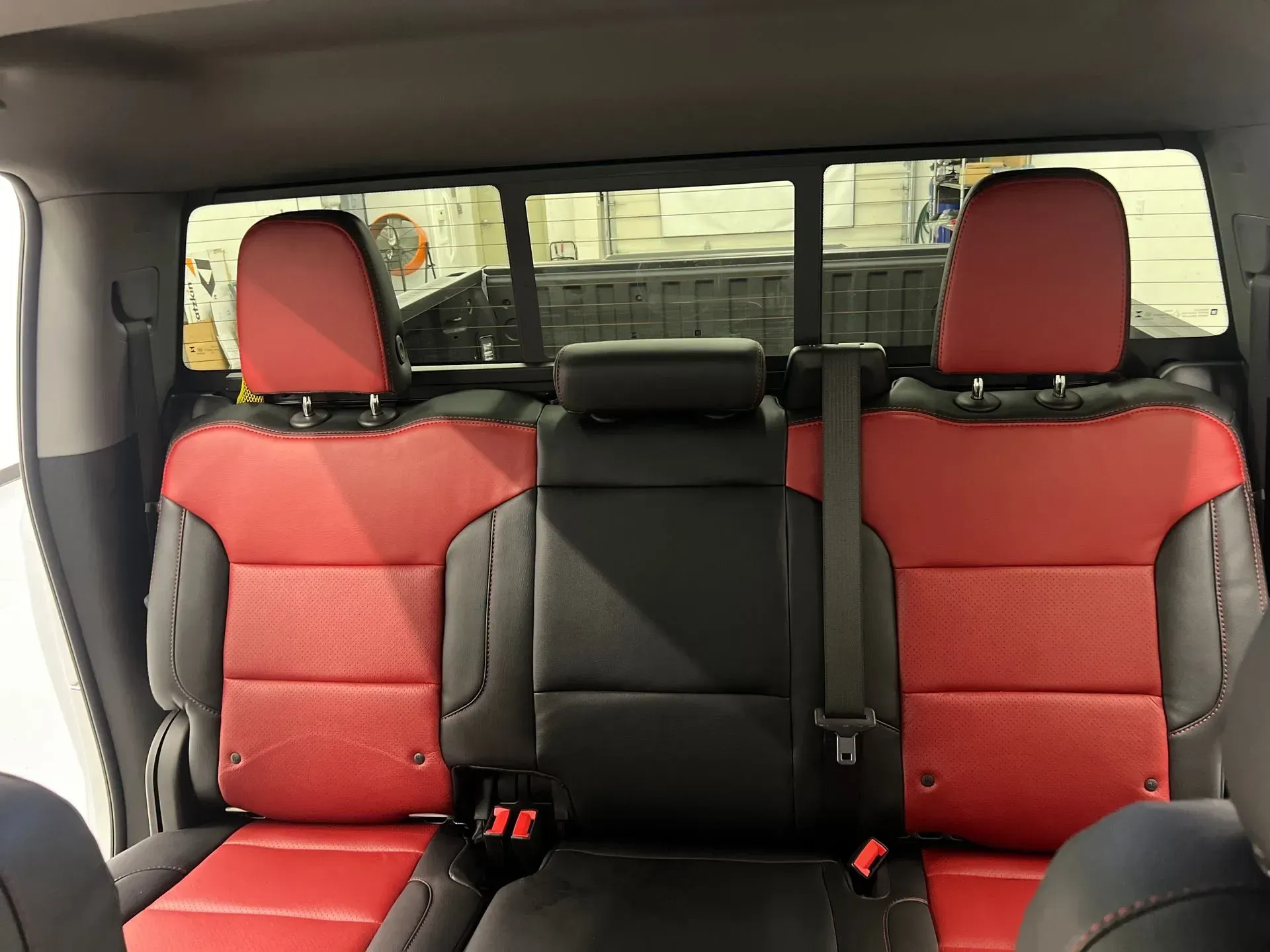 Red and black leather truck backseat with headrests, seatbelts, and a rear window.