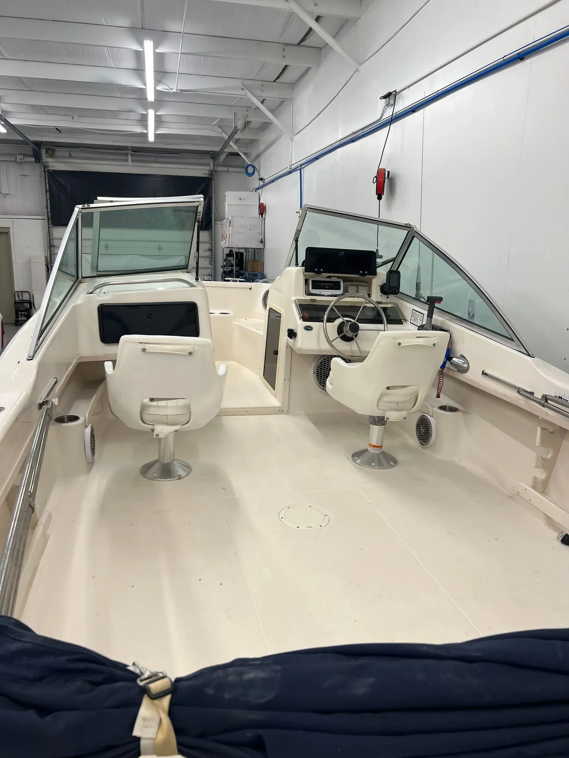 Interior of a boat with two white captain's chairs and a dashboard with navigational equipment.