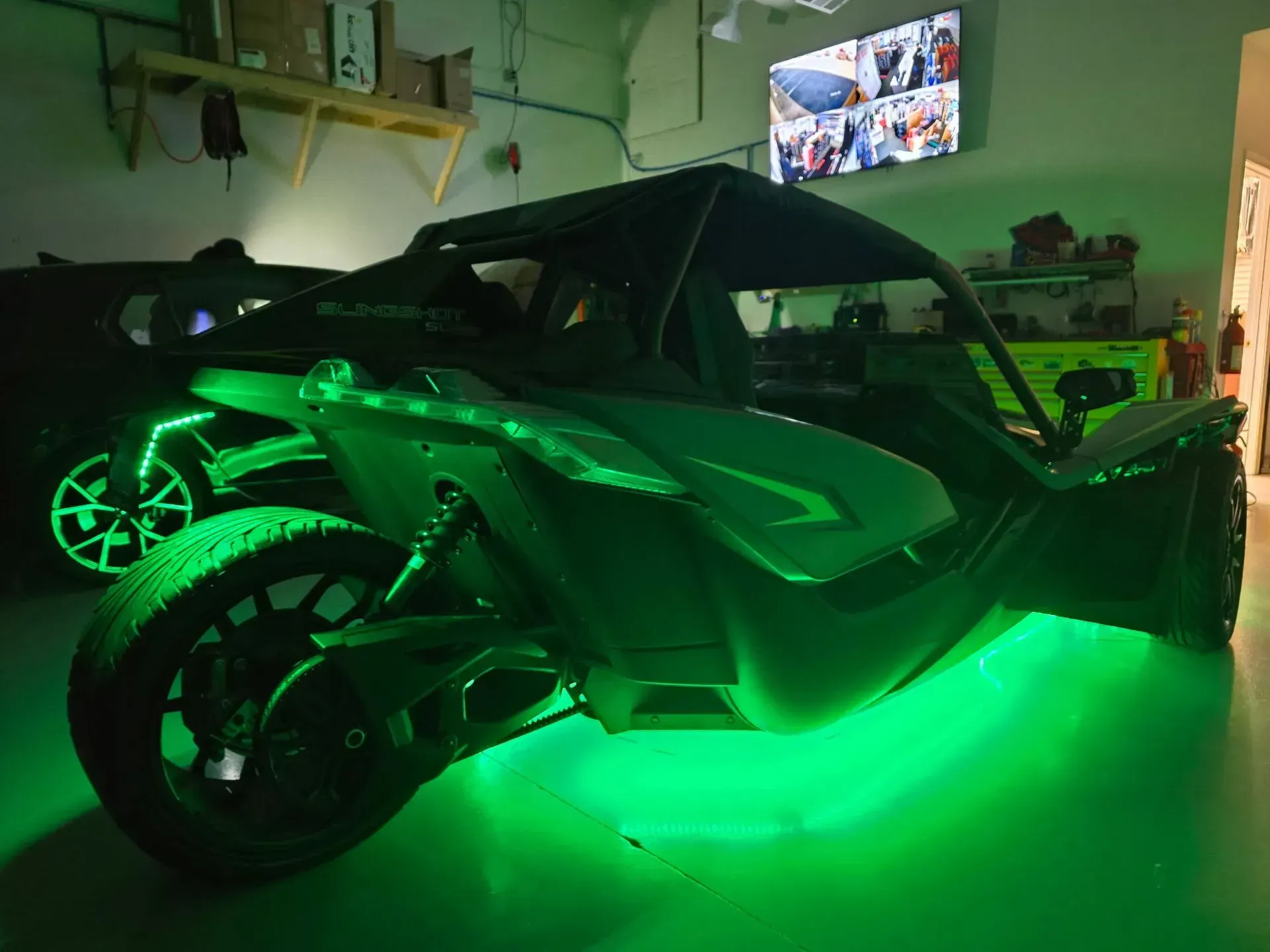 Three-wheeled Slingshot vehicle with green underglow in a garage.