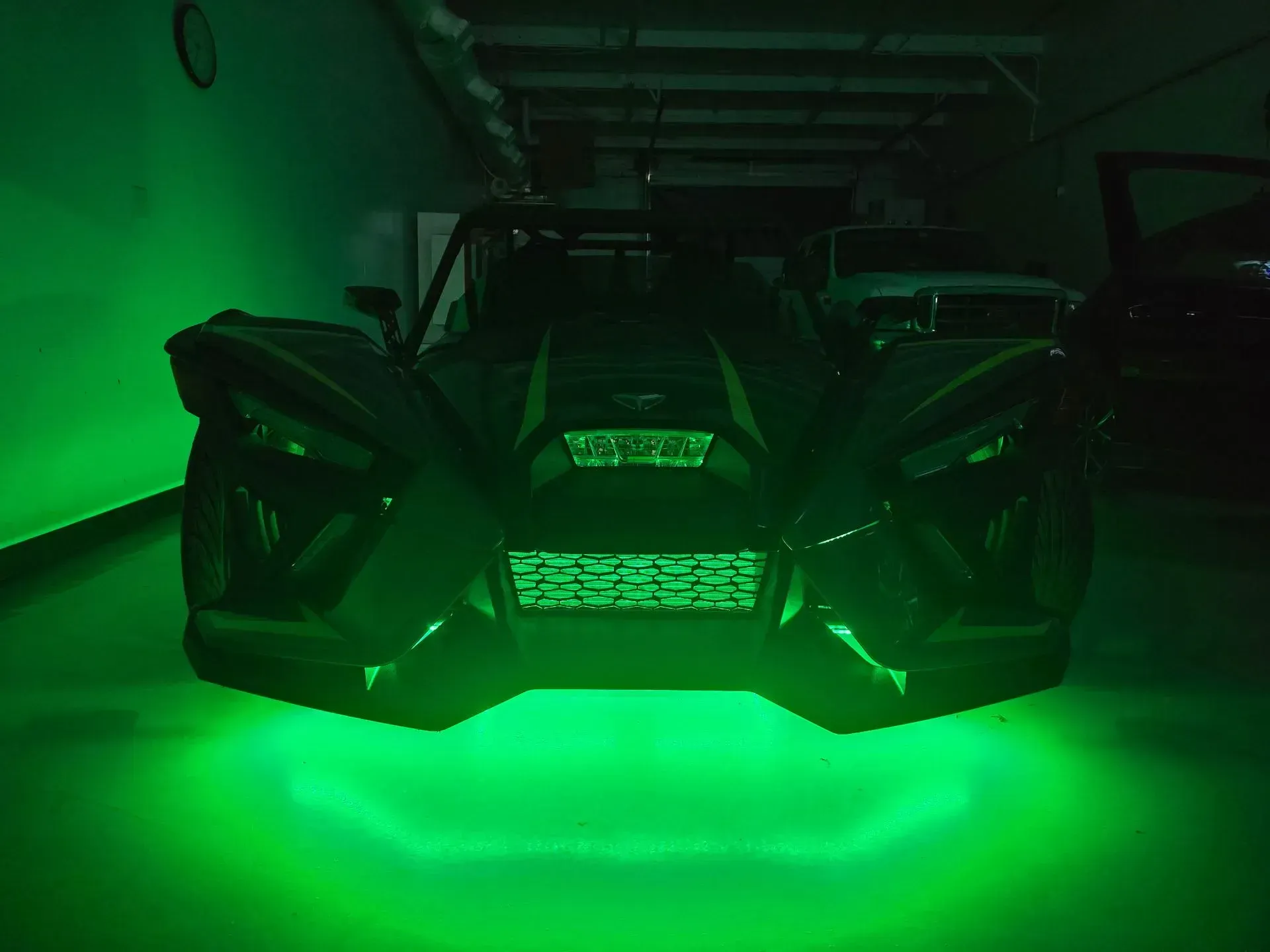 Black three-wheeled vehicle with green underglow in a garage.