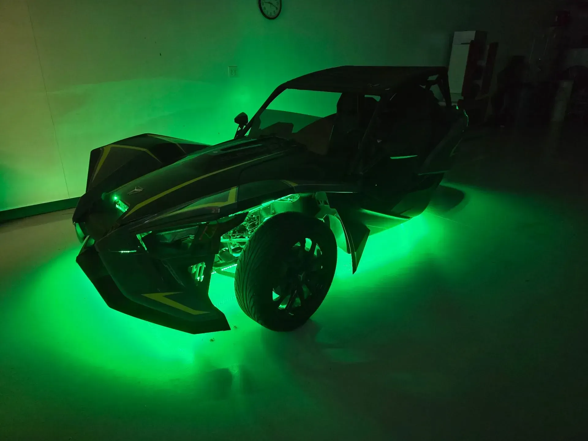 A black Polaris Slingshot three-wheeled vehicle with green underglow parked indoors.