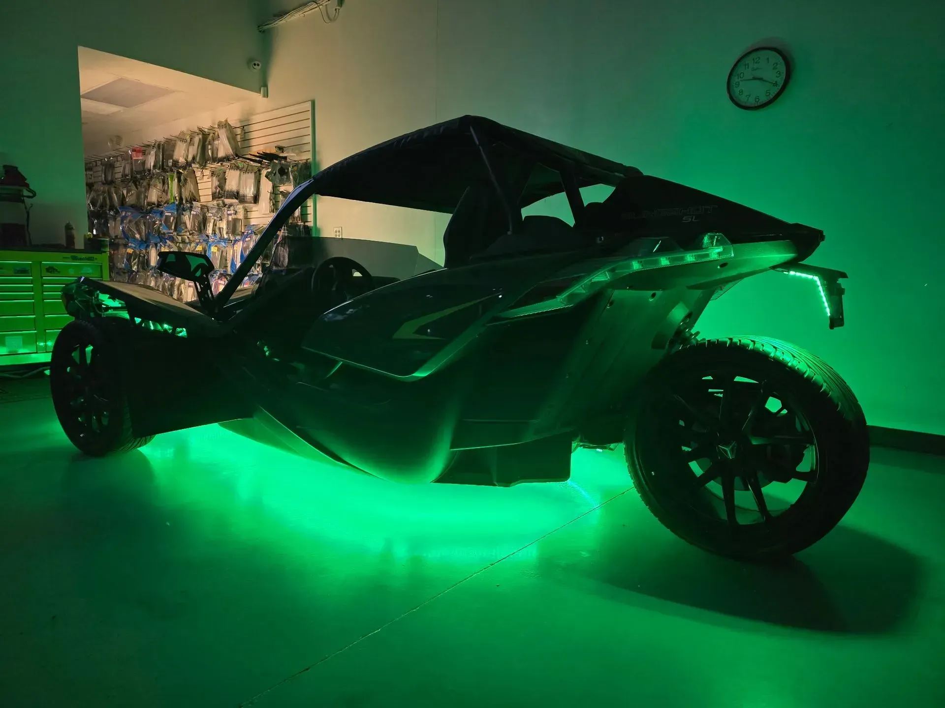 Three-wheeled vehicle with green underglow parked indoors.