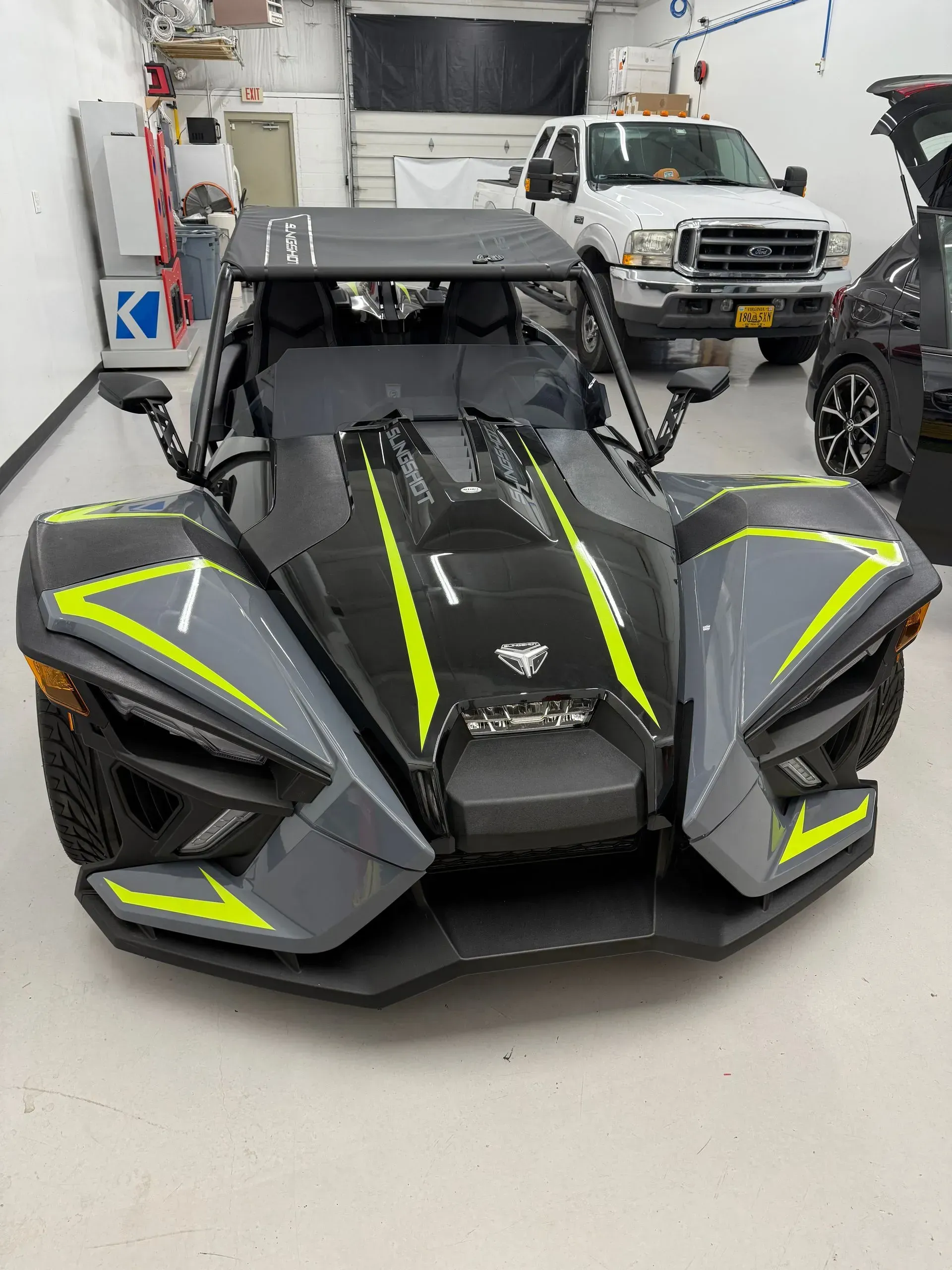Gray and neon green Polaris Slingshot three-wheeled vehicle in a workshop.
