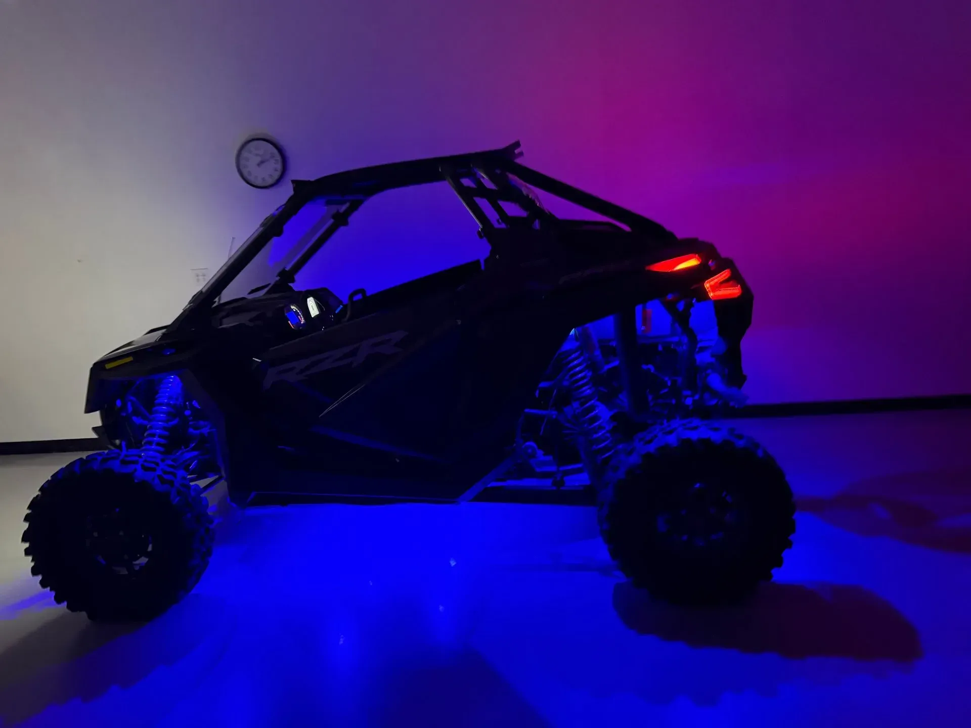 Black Polaris RZR side-by-side with blue underglow, red taillights, lit in a room with a purple background.