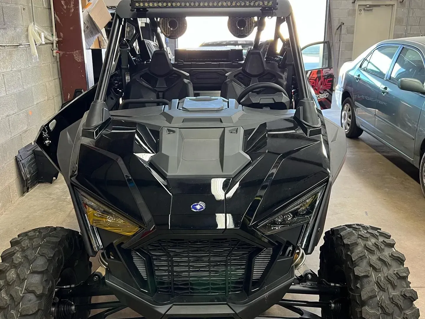 Black Polaris RZR side-by-side vehicle parked inside a garage. It has large tires, and a light bar.