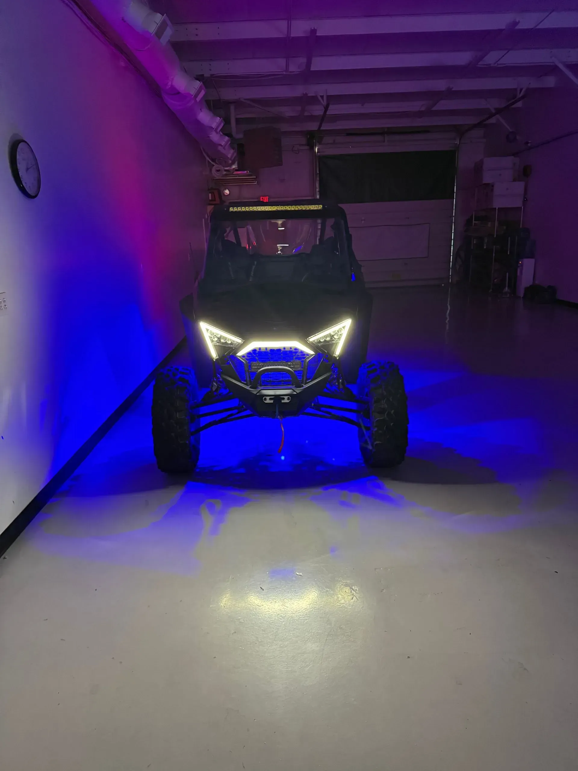 Black side-by-side vehicle with blue and purple LED lights in a garage setting.