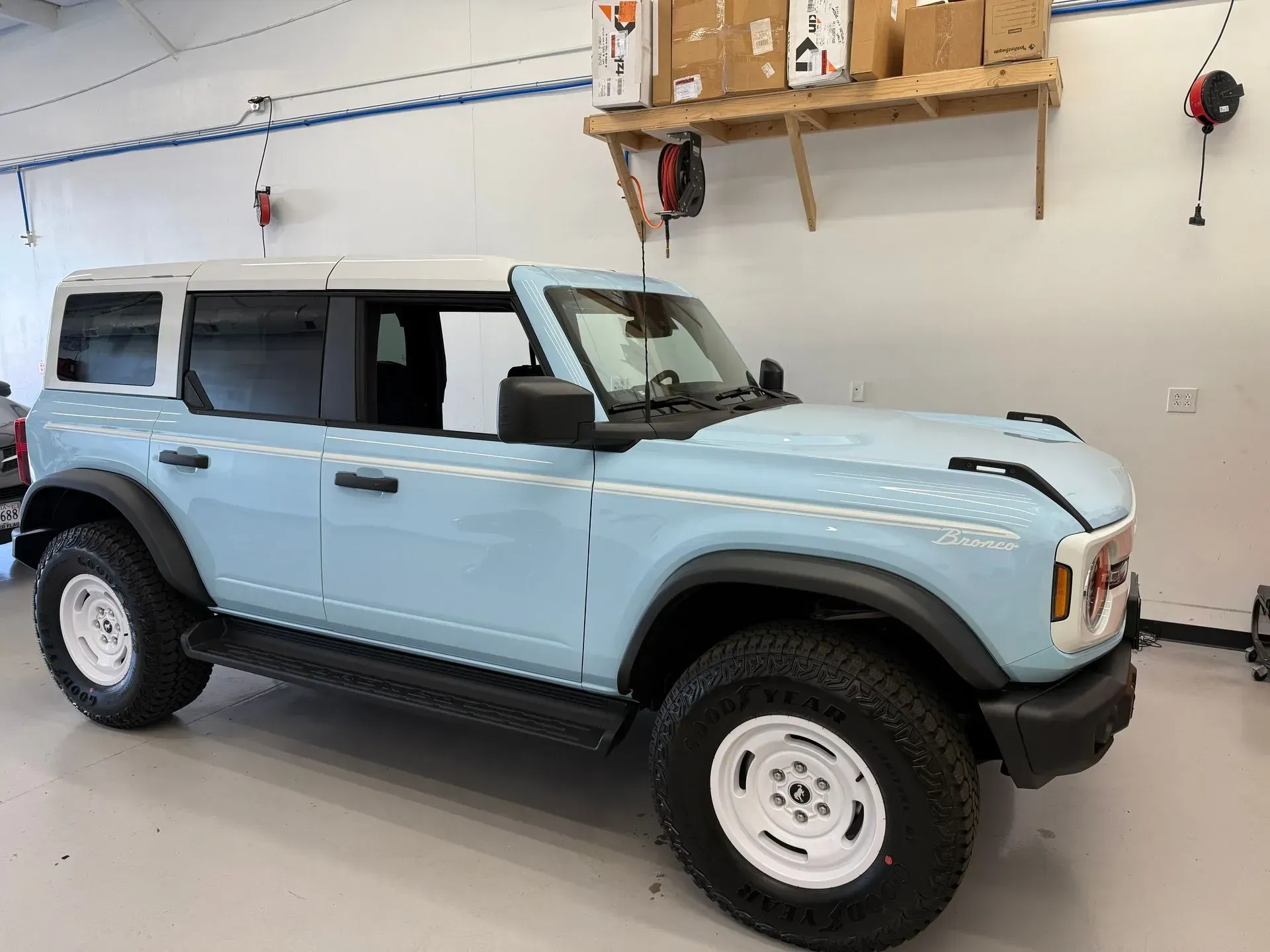 Light blue Ford Bronco with white top and wheels parked in a garage.