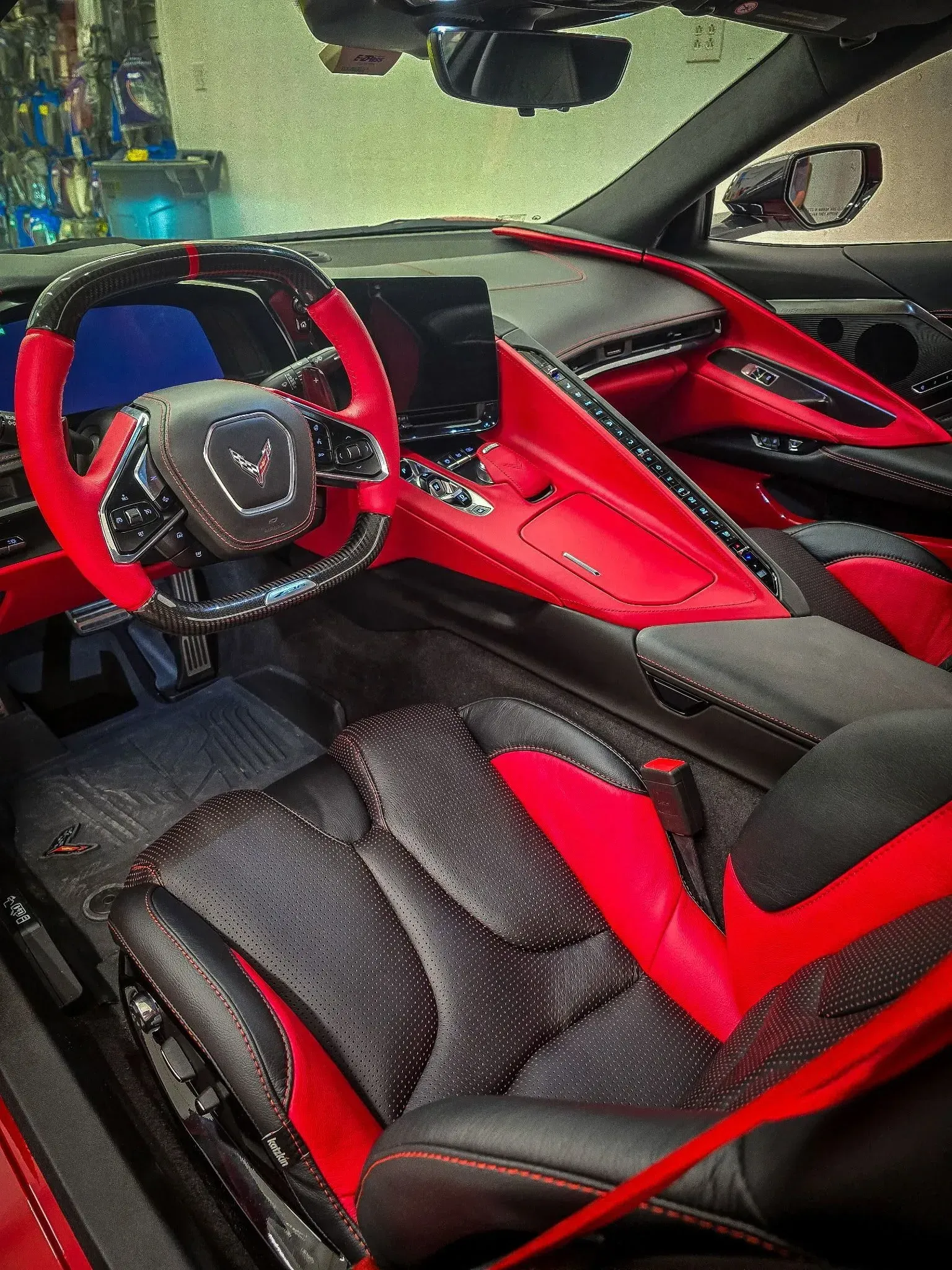 Red and black interior of a Corvette: steering wheel, dashboard, seats, and console.