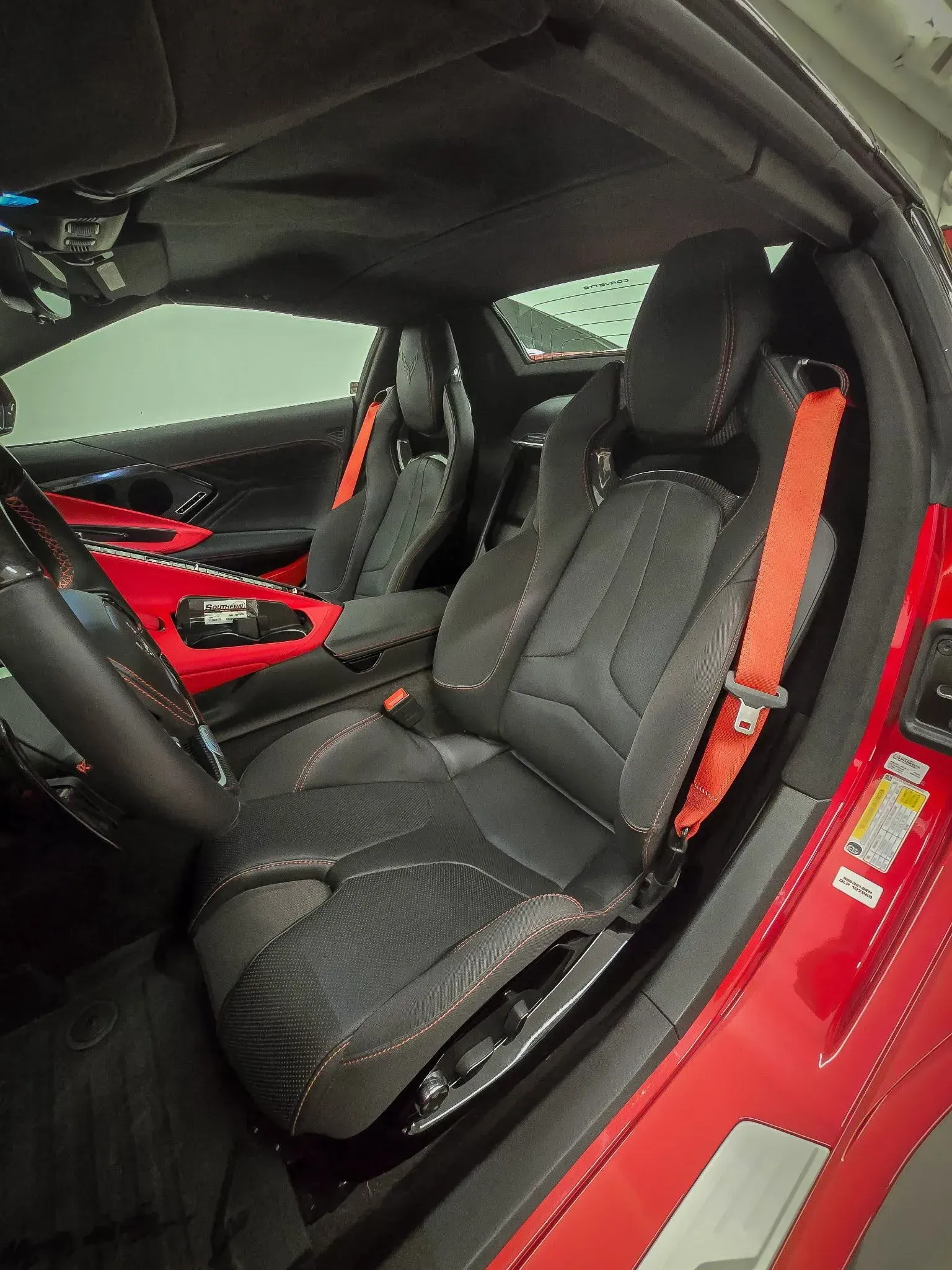 Red Corvette interior with black seats, orange seat belts.
