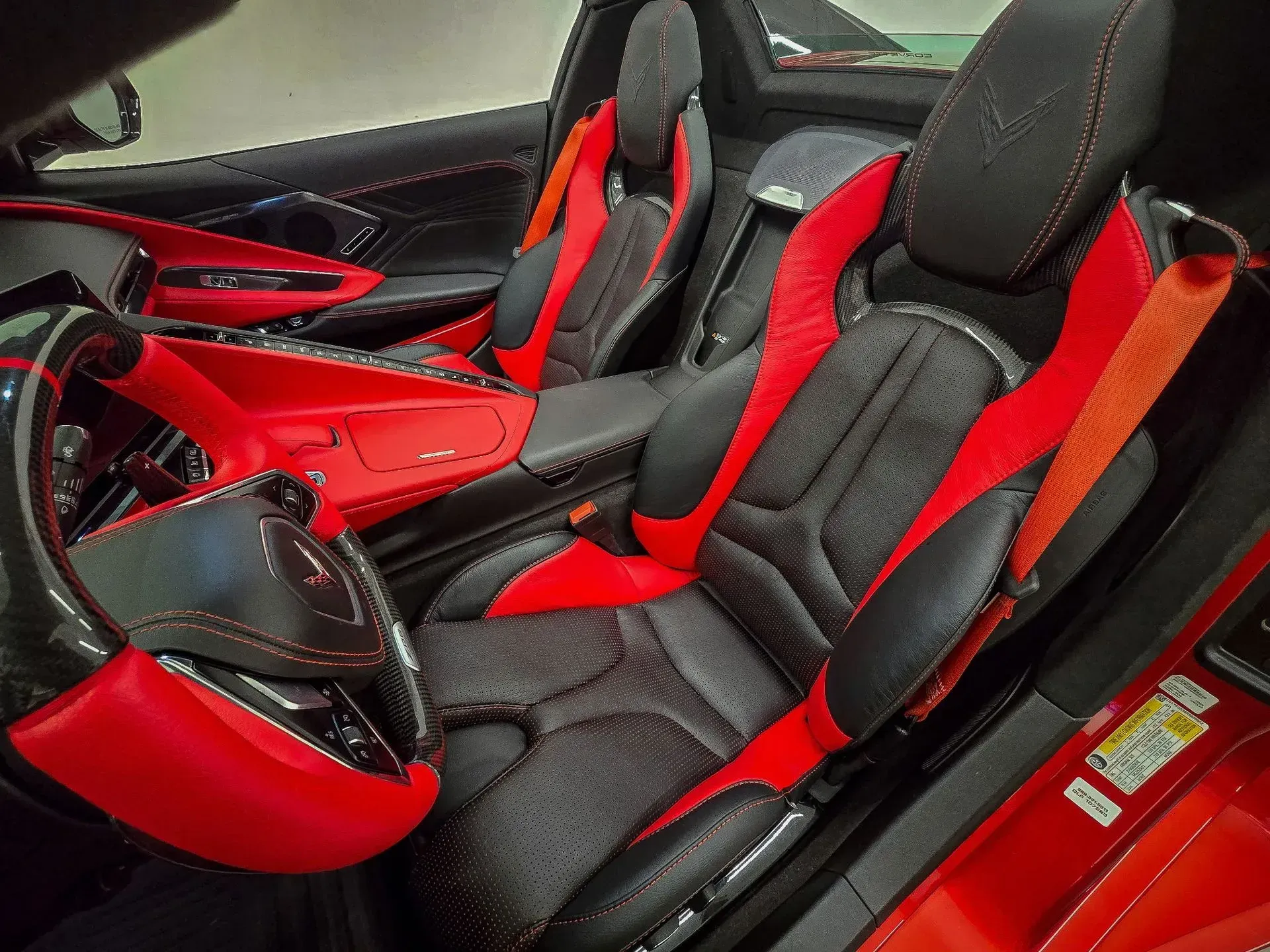 Red and black sports car interior with leather seats, steering wheel, and safety belts.