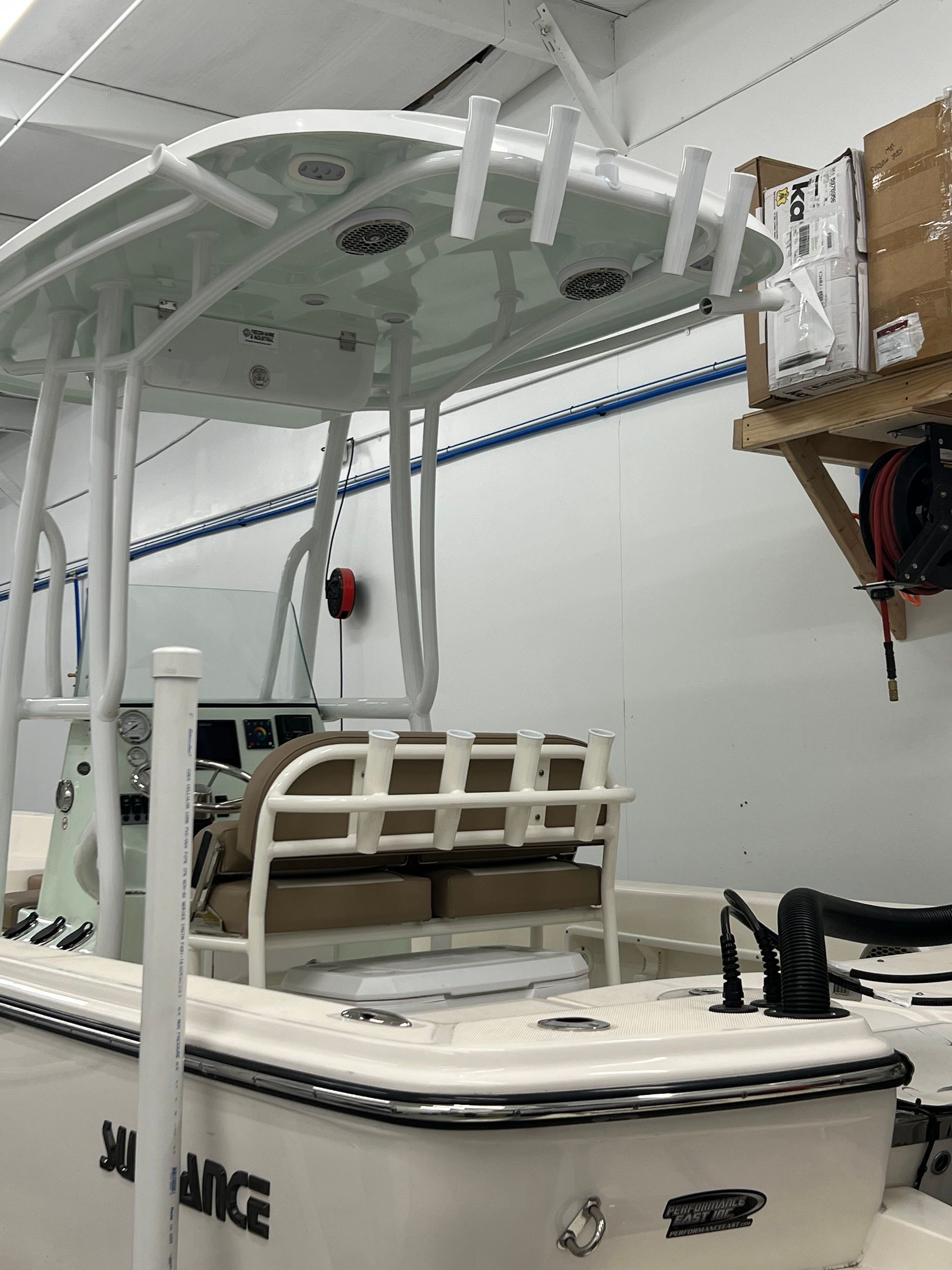 Boat with a white frame, tan seats, and fishing rod holders, inside a building.