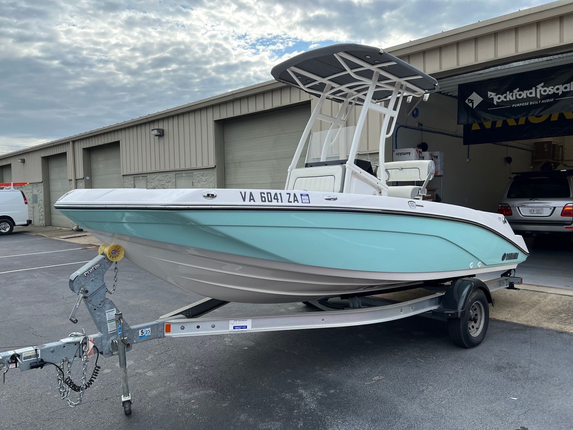 A light blue and white motorboat on a trailer, under a cloudy sky.