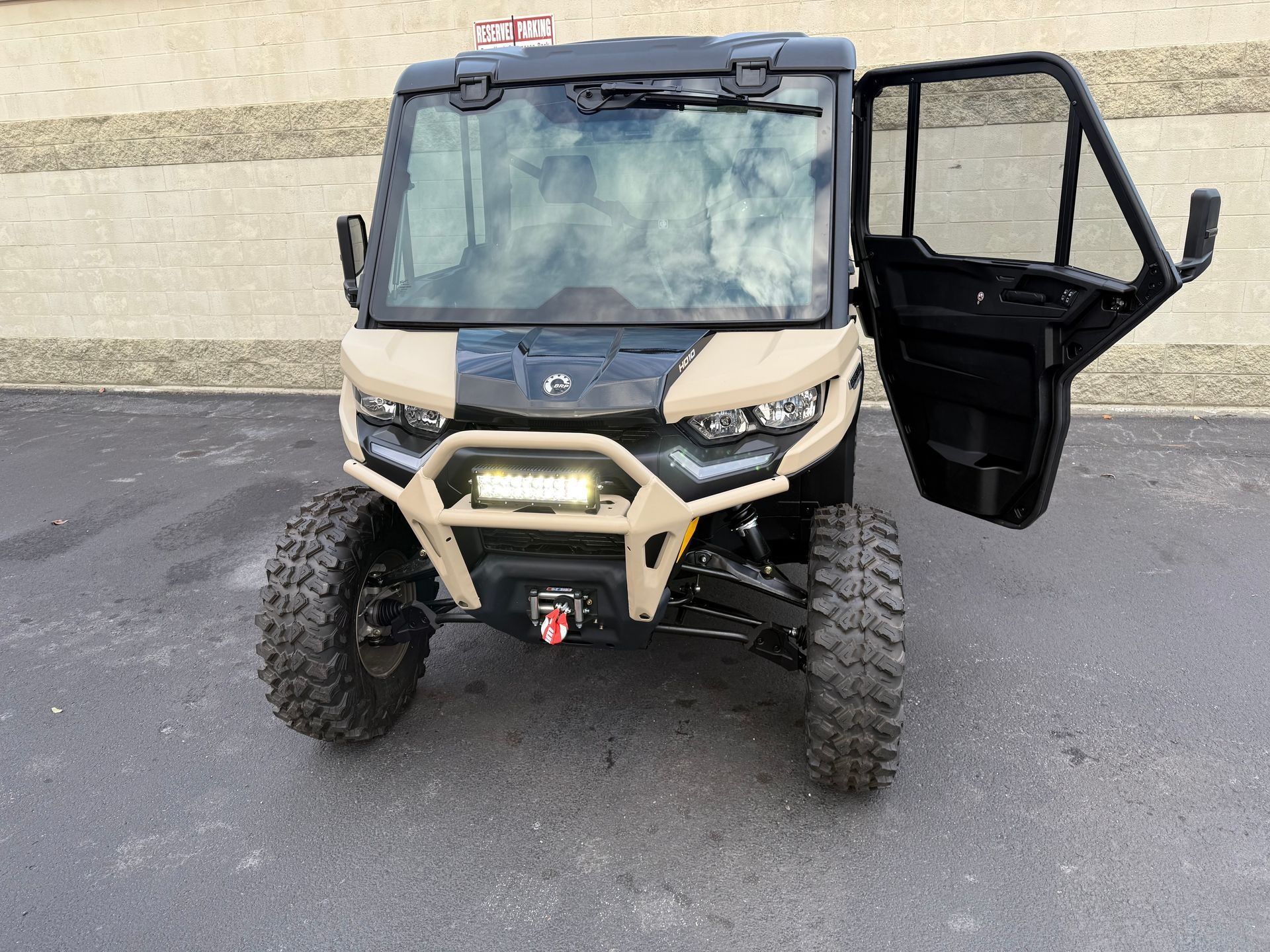 Tan and black off-road vehicle with the driver's side door open, parked on a paved surface.