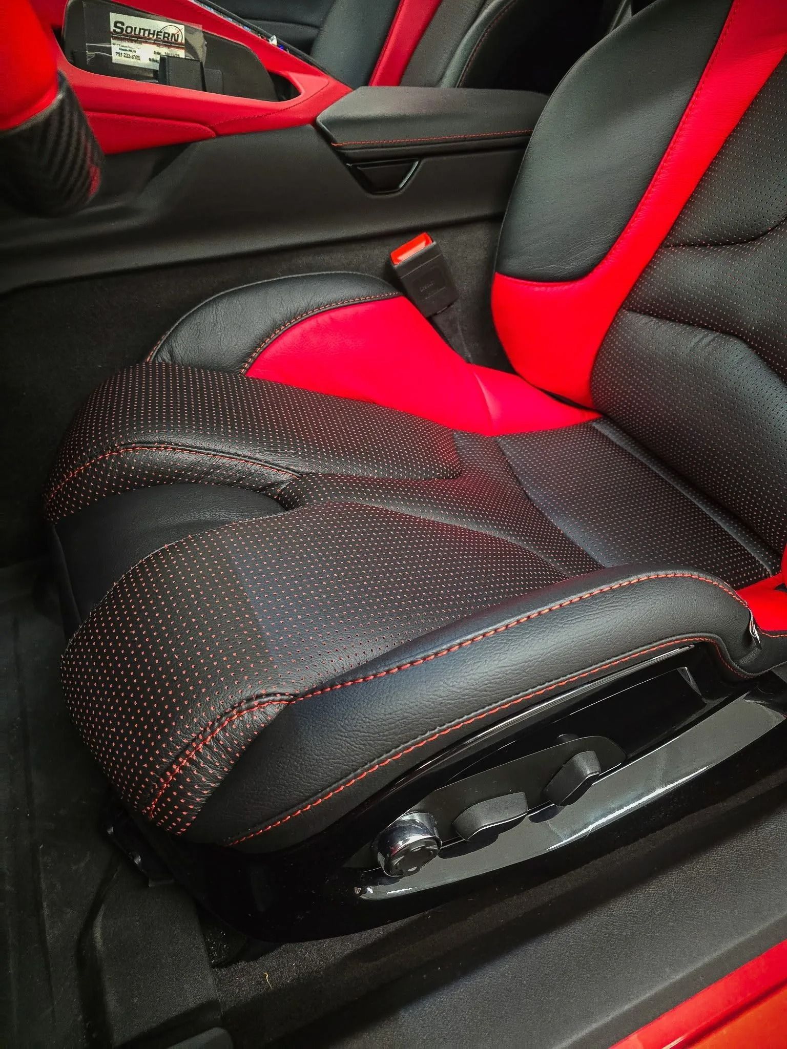 Black and red car seat with perforated design and red stitching. Interior detail.