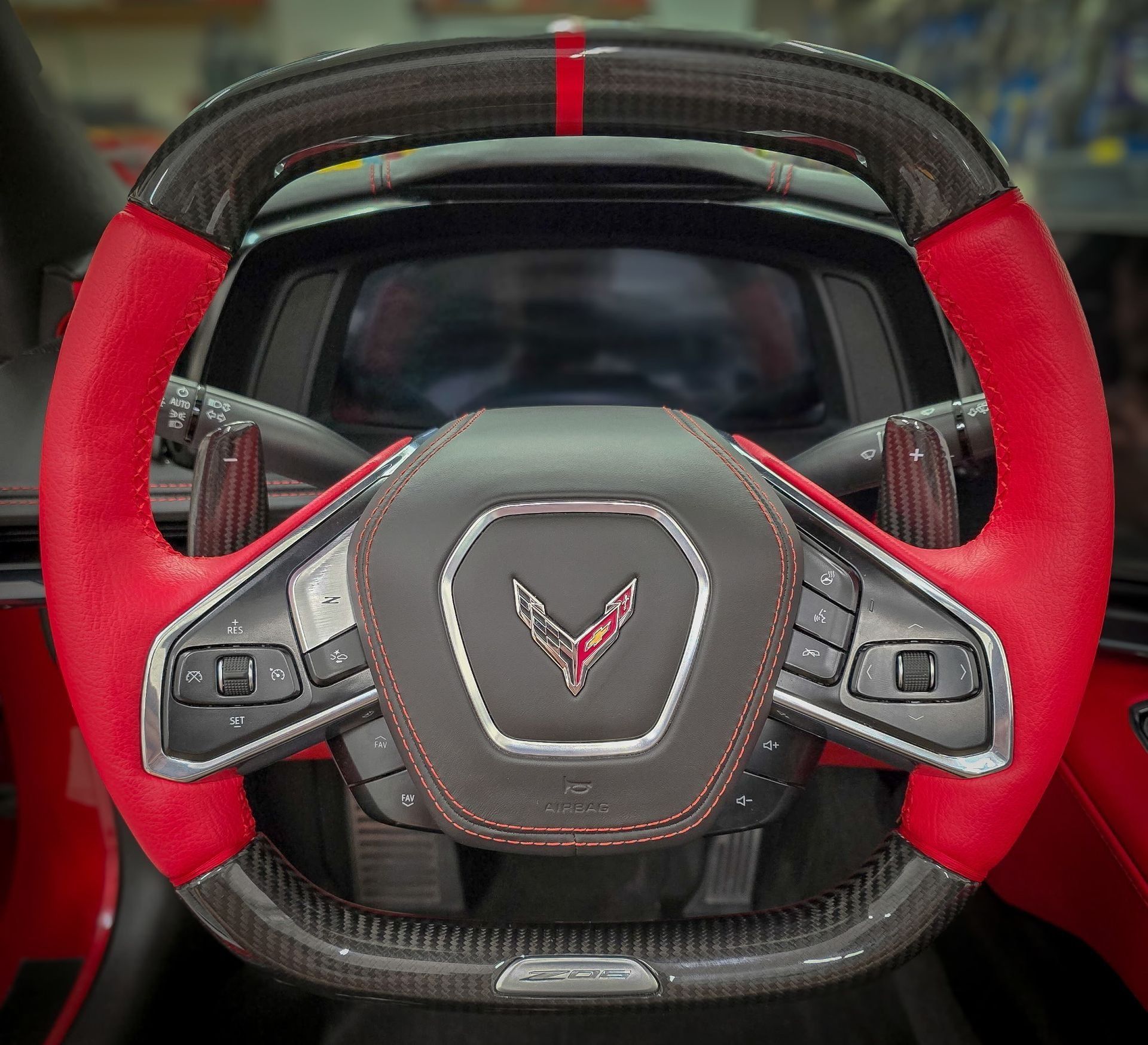 Close-up of a red and carbon fiber steering wheel with black controls in a vehicle.
