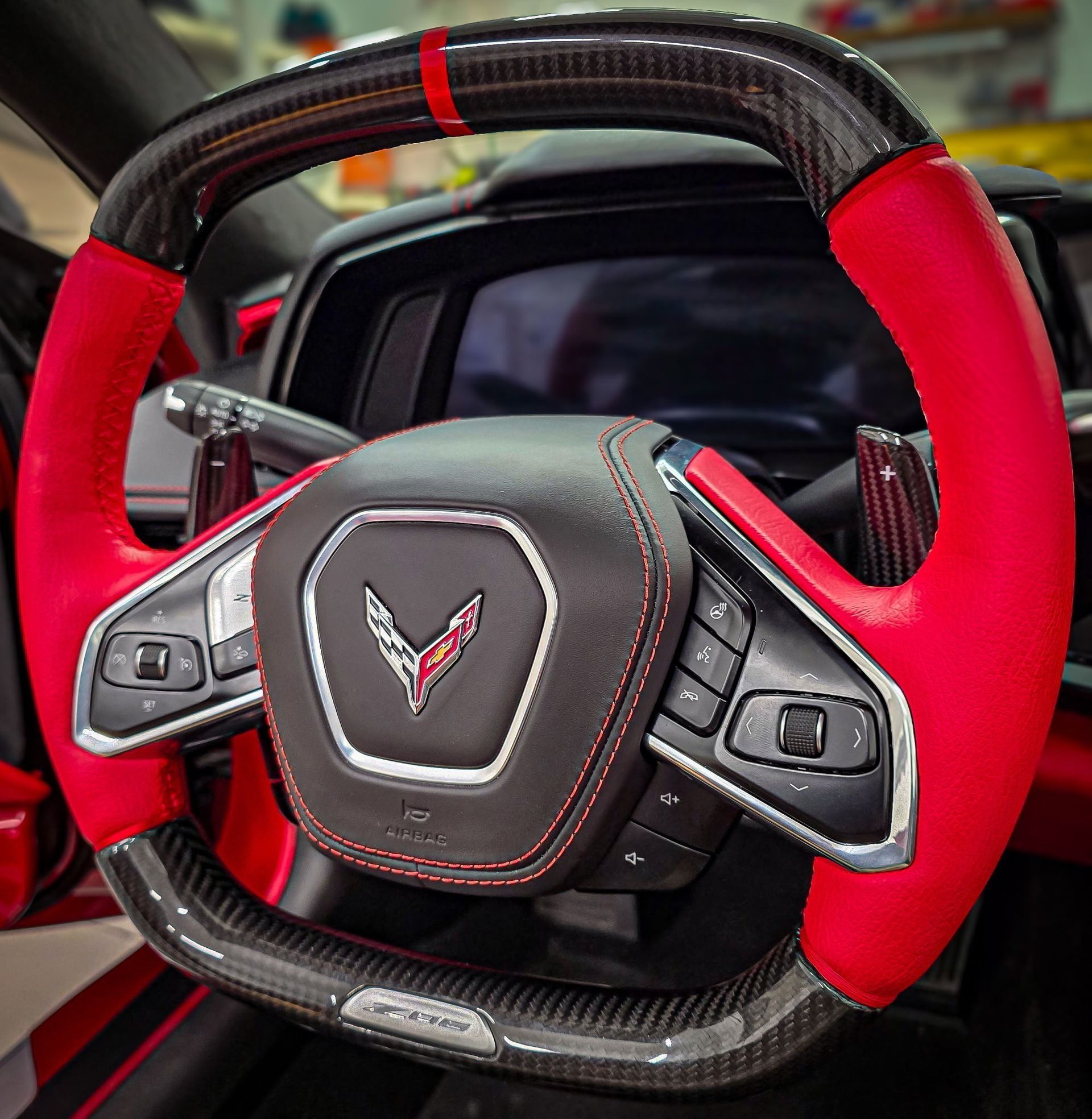 Custom red and carbon fiber Corvette steering wheel with the car's display in the background.