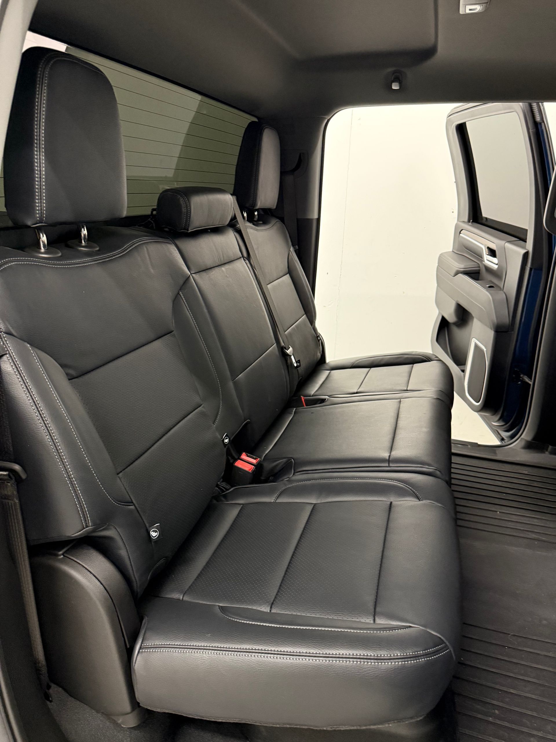 Black leather truck backseat with headrests, open door reveals a dark interior and window.