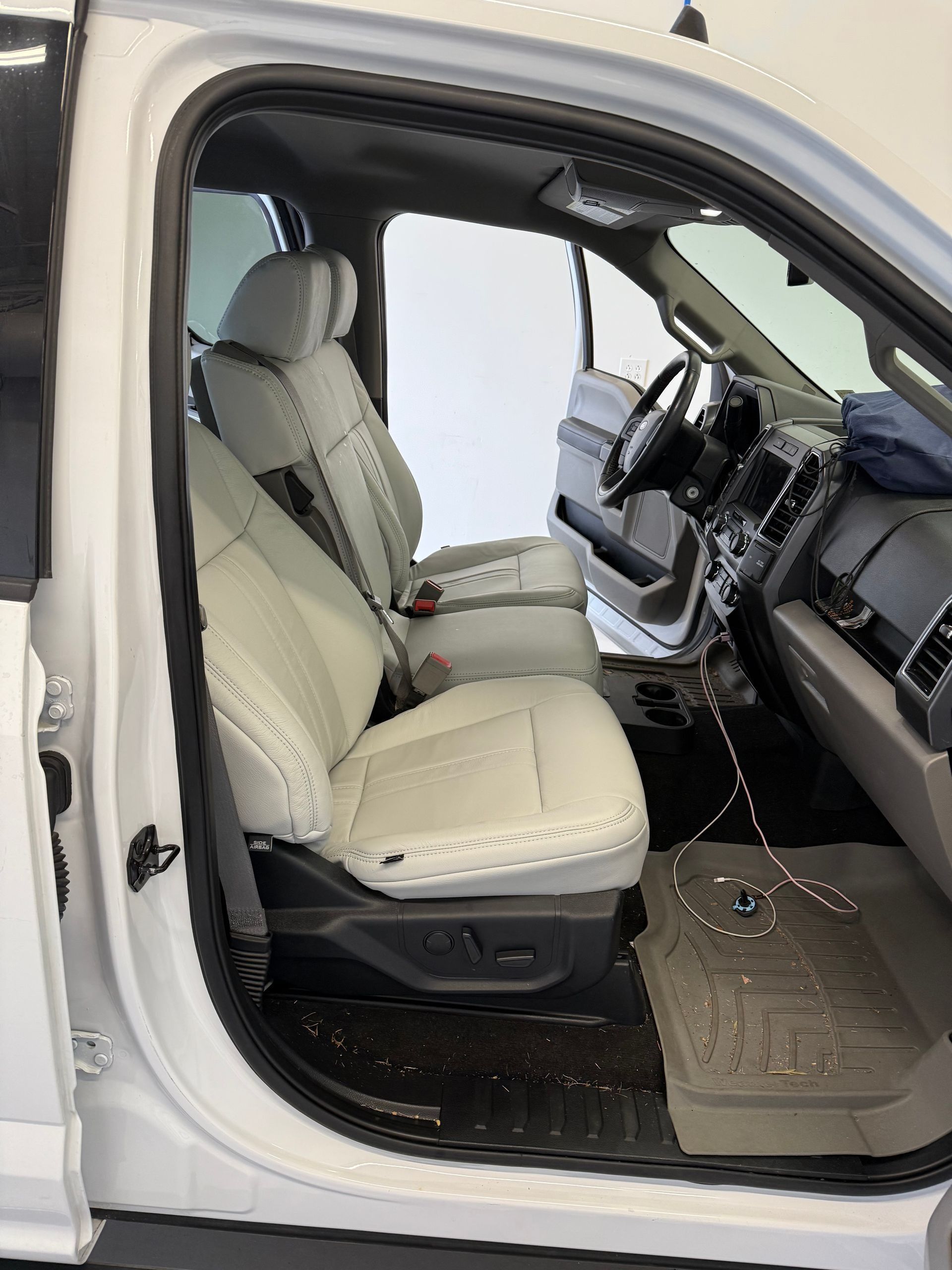White truck interior with light-colored leather seats, black dashboard, and gray floor mat.