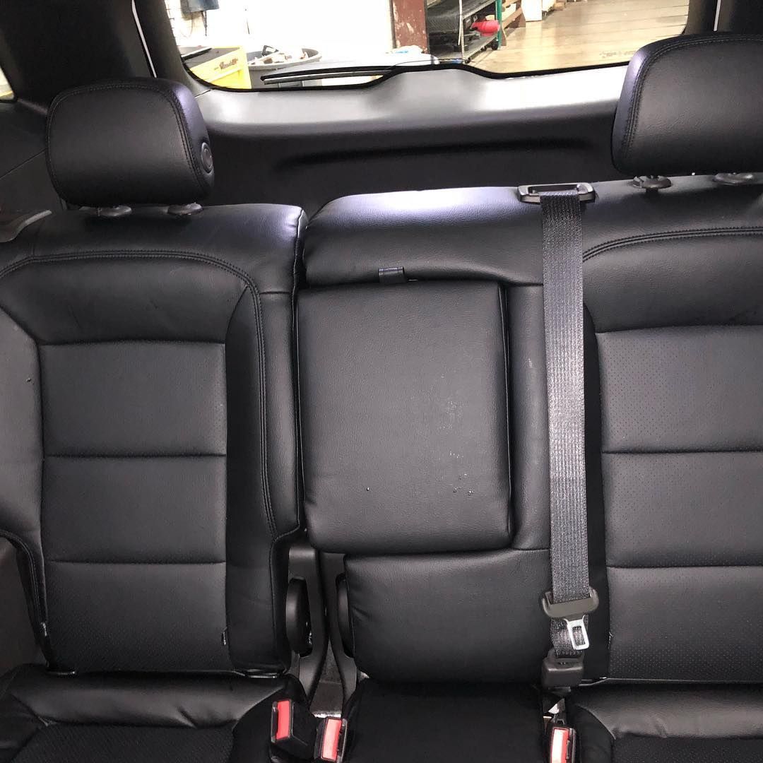 Black leather car seats with headrests and a center armrest. A seatbelt is visible.