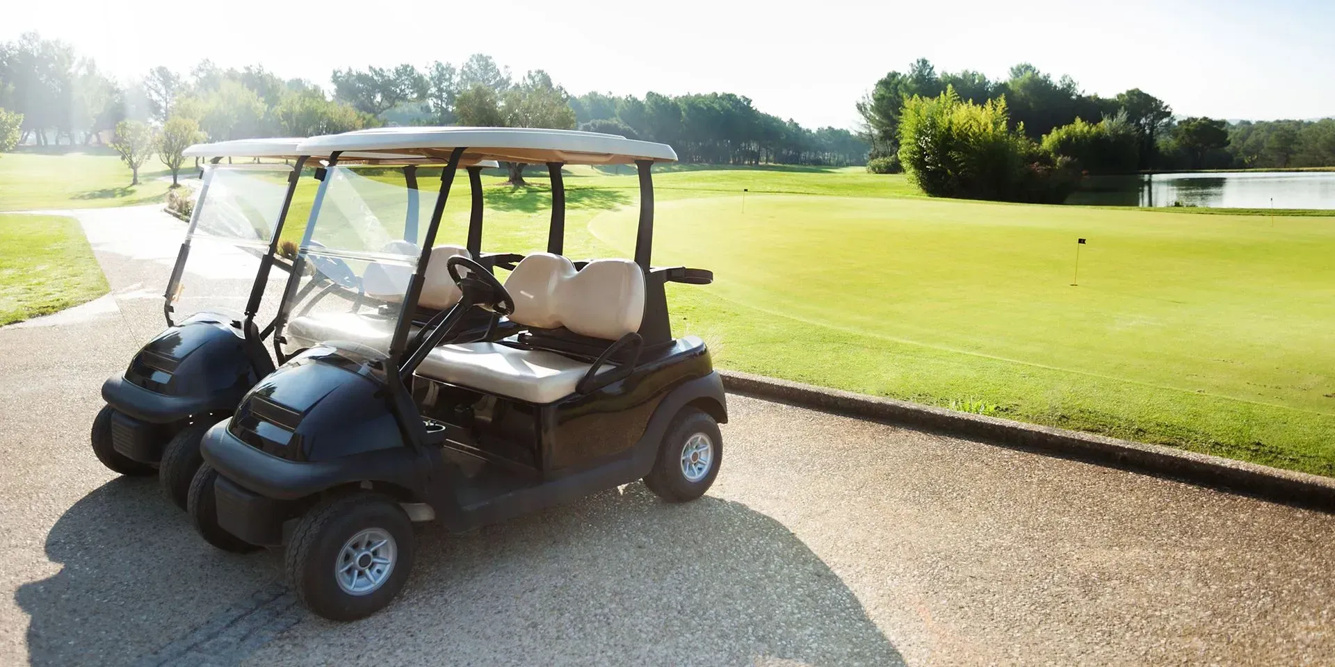 Two black golf carts on a paved path next to a green golf course.